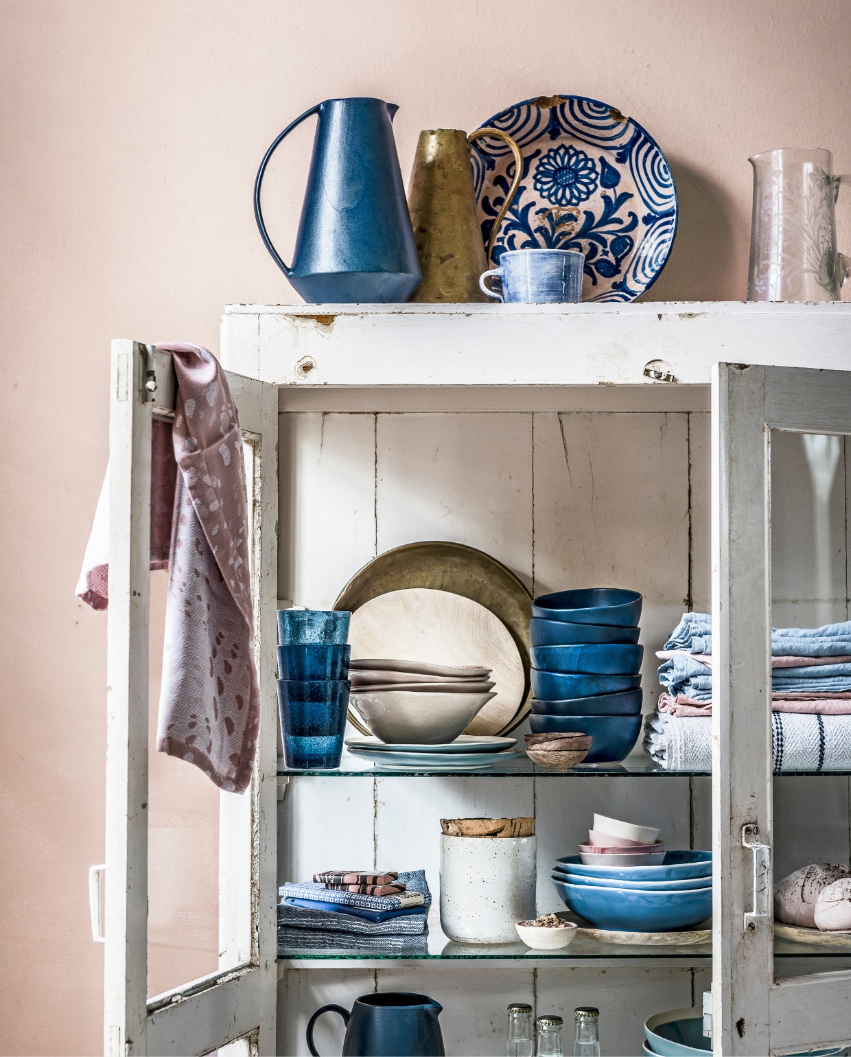 Ecoverf op de wand in kleur Sweetpea van Bauwerk Colour (We Are Wow Makers). Houten vitrinekast met glazen deuren en planken (Raw Materials). Donker-blauwe kan, antieke schaal met bloemenprint, blauwe glazen, organisch gevormde beige kommen, donkerblauwe kommen, klein roze kommetje met suiker, blauwe kan op onderste plank (Stadspaviljoen Noord). Messing kan (Van Dijk &amp; Ko). Blauwe mok, roze theedoek met grafische print, stapel roze schaaltjes in blauwe schalen (Maison NL). Antieke glazen kan met geslepen bloemmotief (Brechtje Olsthoorn Interiors). Borden van mangohout, drie opgestapelde blauwe schalen (Loods 5). Kleine houten kommetjes (Nijhof). Blauwe borden met witte rand, blauwe schaal met witte rand op onderste plank (www.vtwonen.nl) Wit canvas tafelkleed met blauwe streep (Six and Sons). Blauwe en roze linnen servetten (H&amp;M Home). Blauwe theedoeken met witte strepen (Eland&amp;vanderHelst). Witte pot van keramiek met kurken deksel (Restored). Overig privébezit. vtwonen 08-2017 | styling Danielle Verheul | Fotografie Sjoerd Eickmans
