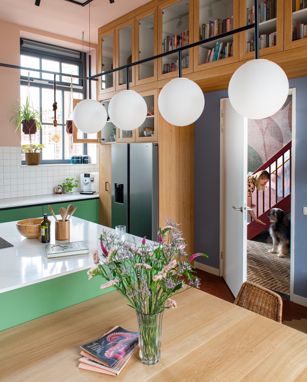 Annemieke in de hal van haar herenhuis. Muurverf en verf plafond S1510-Y90R van Histor. Keukenkasten in RAL 6011 van Sikkens. Wandtegels Mosa van Classics Kho Liang Ie. Tafel Jouke Bouwhuis. Witte hanglamp Audo Copenhagen, hanglampen aan stang zelfgemaakt. Eikenhouten maatkast Studio Jasper. Vloer hal Bonte. Verf trap Old Red van Pure & Original. Behang Flora van Selected Wallpapers. Overig onbekend. vtwonen special binnenkijken 121-2023 | productie De Binnenkijkers | styling Jeske Weel | fotografie Caroline Coehorst