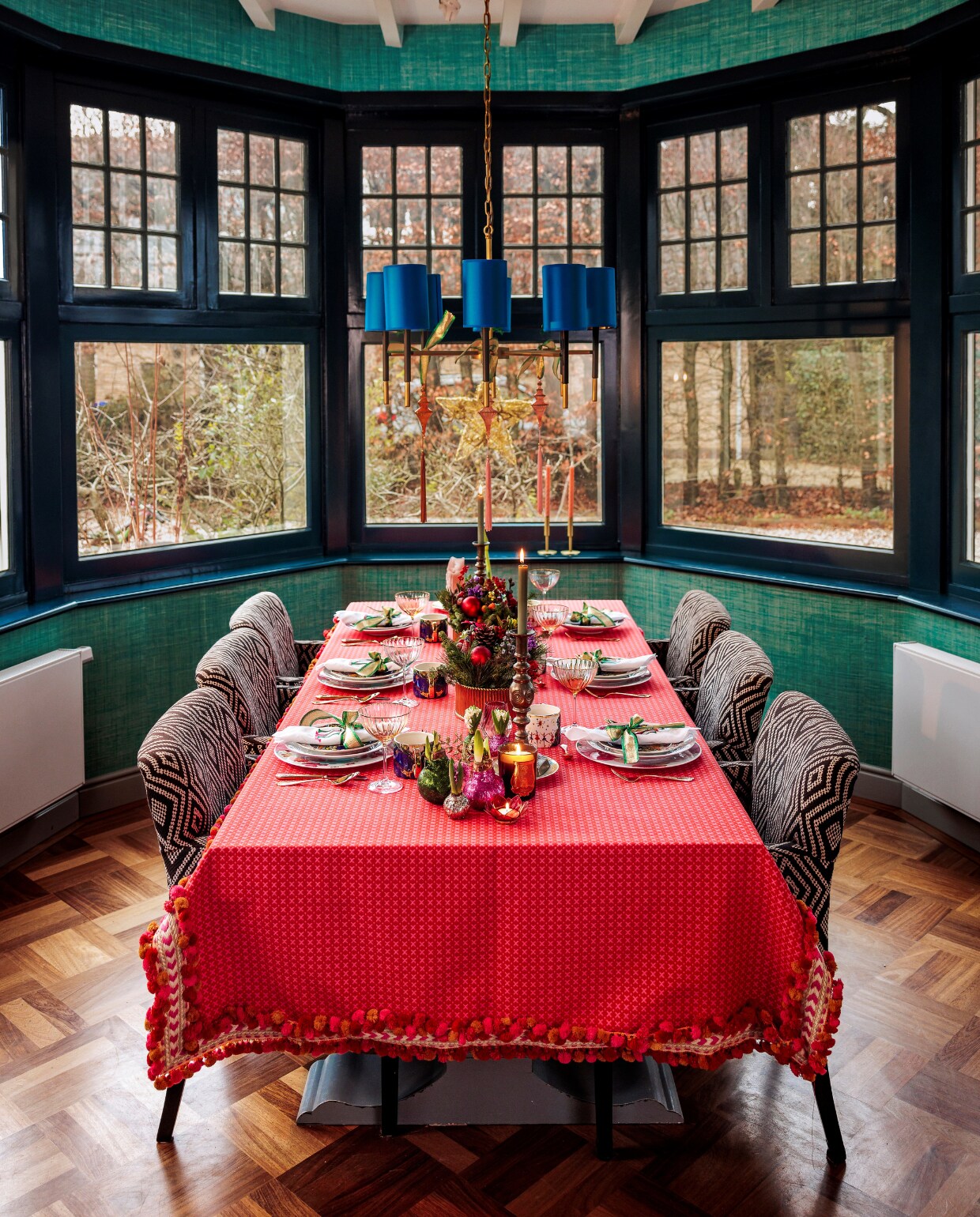Behang Thibaut, verf kozijnen Hague Blue van Farrow &amp; Ball, hanglamp Marie Martin. Tafelkleed gemaakt door Gordijnmakers Hilversum met stof van Schumacher, stoelen Interiors Dmf. Kerststukken en bloembollen Eindeloos Bloemen. Overig onbekend. vtwonen 13-2023 | styling Ilona Jongepier | fotografie Ernie Enkelaar