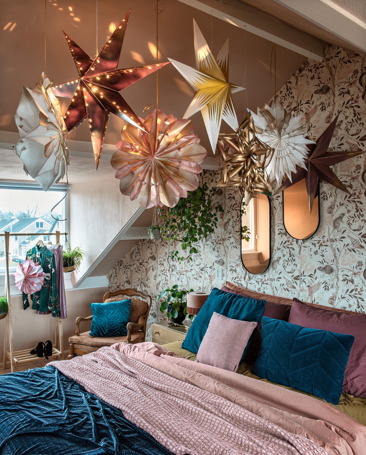 De kerststerren zijn van Ikea en zelfgemaakt met boterhamzakjes. Behang met ratjesdessin Mineheart. Roze plaid en bedlinnen Suite 702. Spiegels en petrol sprei van stof van Kwantum. Kussens: op stoel onbekend, links Boer Staphorst, rechts Volt Studio, klein Jysk. Kastje en stoel kringloop. Lampje Skylerstore. Kledingrek Action, blouse Up to date mode, rok kringloop, schoenen H&amp;M. vtwonen 12-2020 | styling Mindy Schoor | fotografie Ton Brouwer | productie en tekst Monique van der Pauw