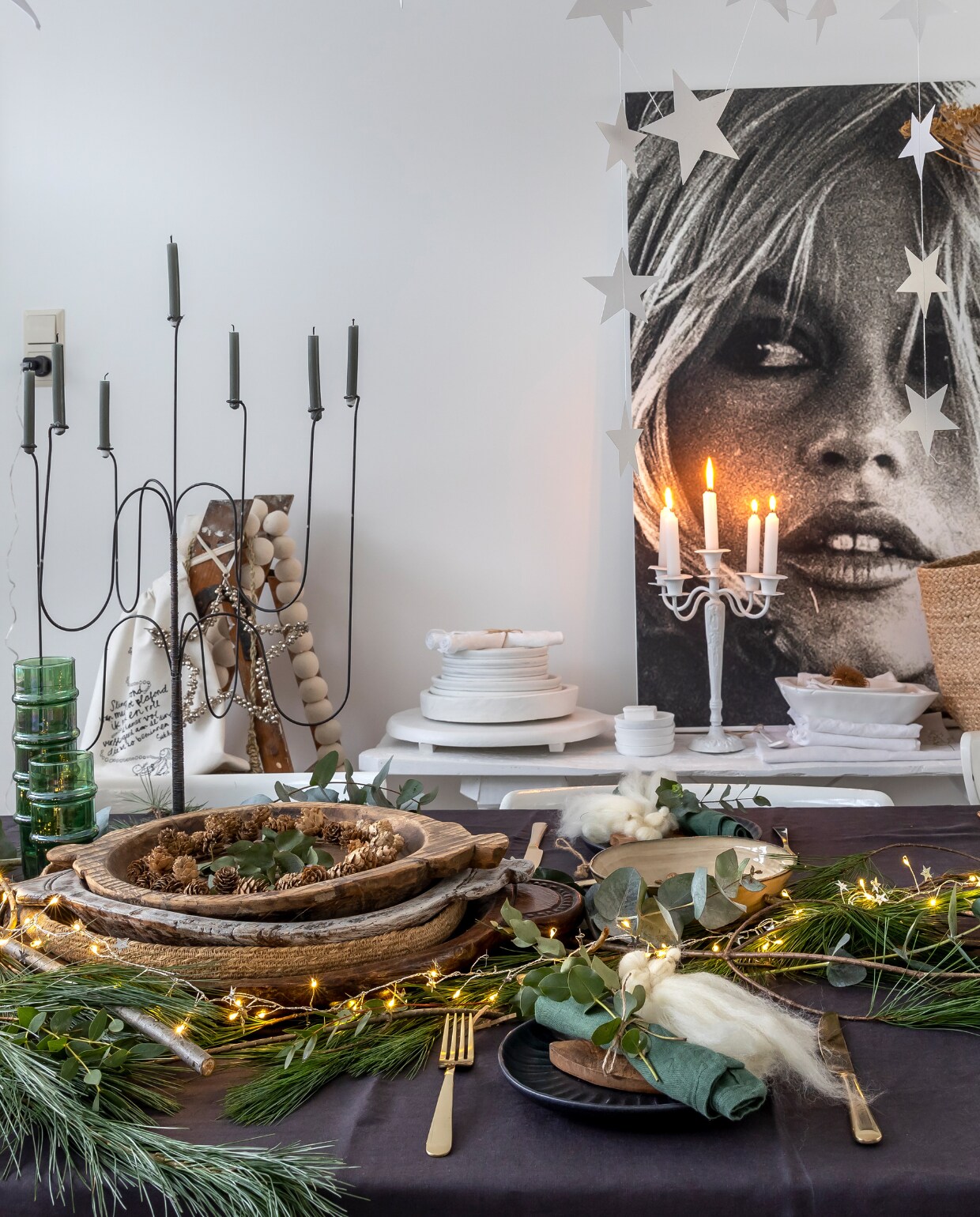 IJzeren zevenarmige kandelaar De Tuinkamer brocante. Mand H&amp;M. Witte ijzeren kandelaar, eetkamerstoelen, houten schilderstrap Marktplaats. Grijs tafelkleed H&amp;M. Gouden bestek Albert Heijn en Sissy-Boy. Witte houten schalen Action (zelf geverfd). Tas Sukha. Groene takken markt. Houten schalen Marktplaats en kringloop. Groene glazen Household Hardware. Groene servetten Søstrene Grene. Zwarte borden Sissy-Boy. Beige schalen Xenos. Wijnglazen kringloop. Sterren Aliexpres. Engelen op borden zelfgemaakt. Overig onbekend. vtwonen 13-2023 | fotografie Henny van Belkom