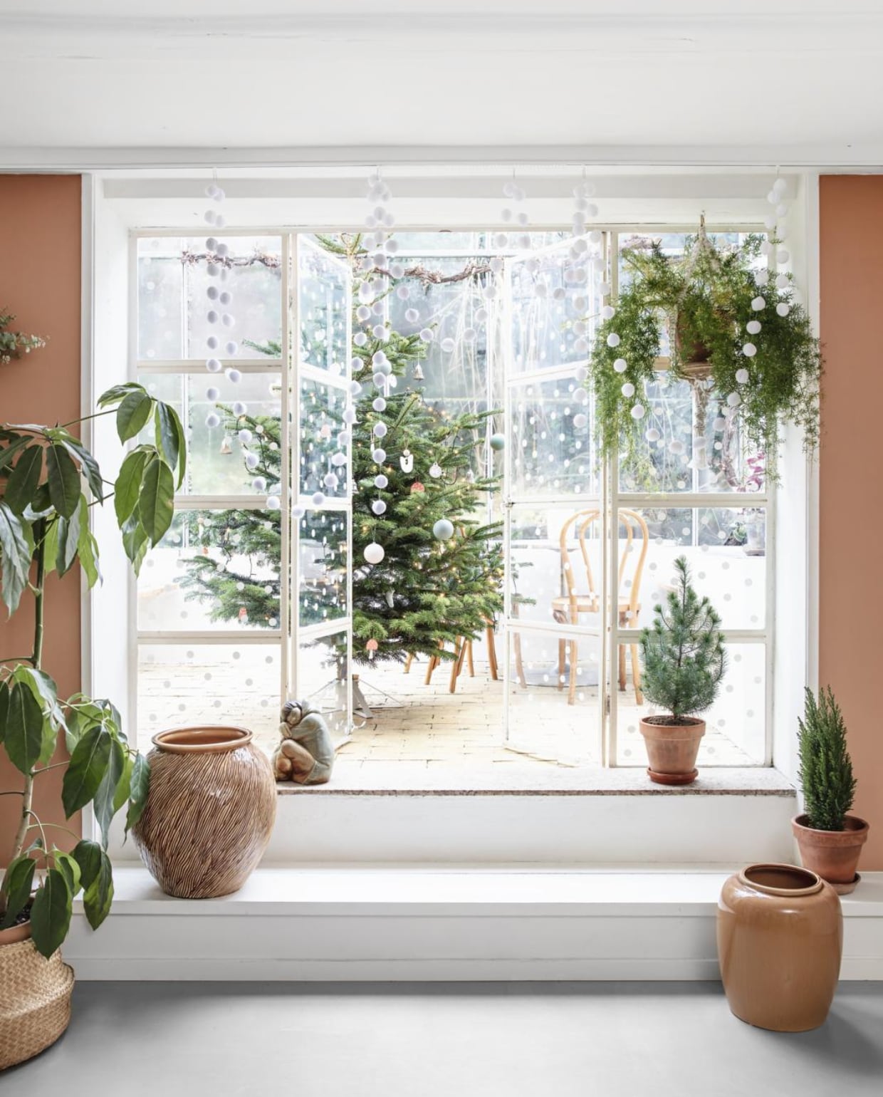 De keuken en eetkamer bevinden zich in het souterrain van het huis en geven toegang tot de serre waar het gezin het hele jaar door te vinden is. De overgang tussen het eetgedeelte en de orangerie is weelderig gedecoreerd met groene planten (hellonature.dk). Op de muur kleur Terra di Siena van Flügger. Op de glazen deuren heeft Rikke een decoratie van sneeuwvlokken aangebracht. vtwonen 13-2019 | styling Rikke Graff Juel | fotografie Christina Kayser O.