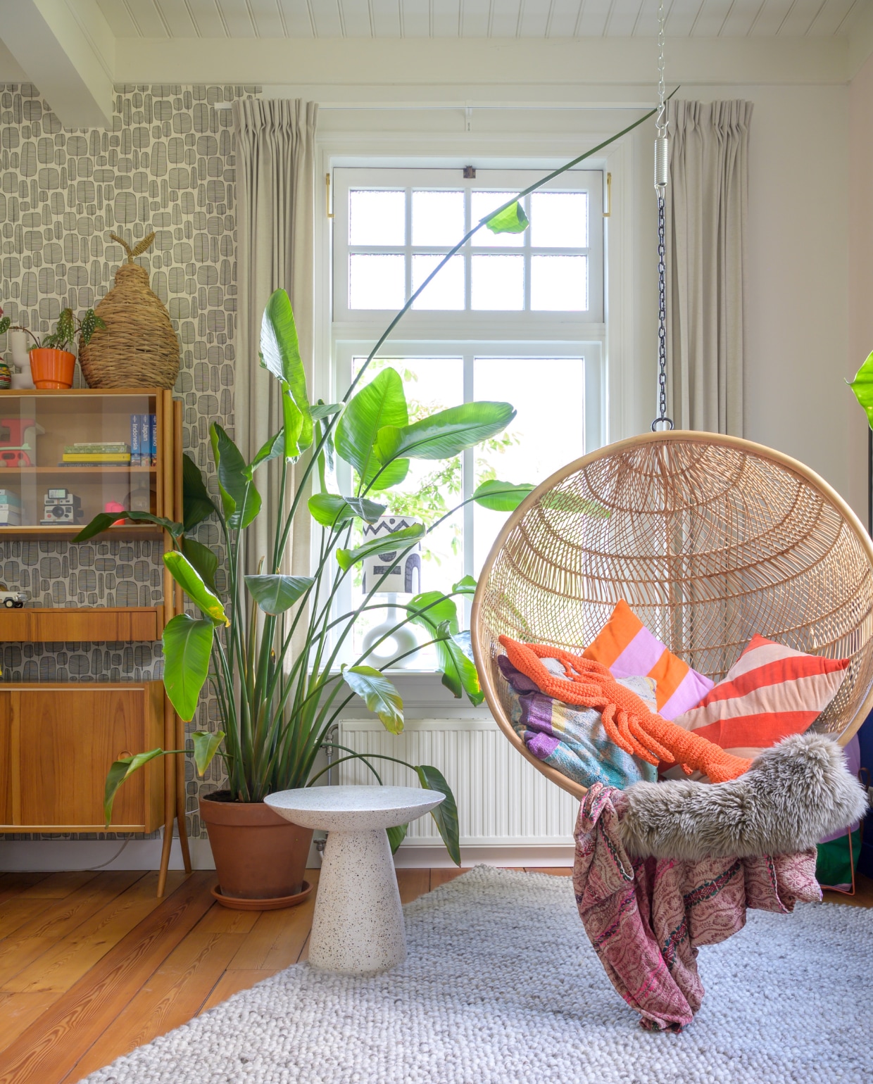 Behang MissPrint. Gordijnen Karwei. Vintage kast Marktplaats. Plant en vloerkleed Ikea. Bijzettafel Loods 5. Hangstoel HKliving, kussens Van Verre, Afroart en HKliving, plaid Van Verre. Lamp in vensterbank met zelfgemaakte kap Urban Nature Culture.   vtwonen special binnenkijken 121-2023 | fotografie Trui Heinhuis