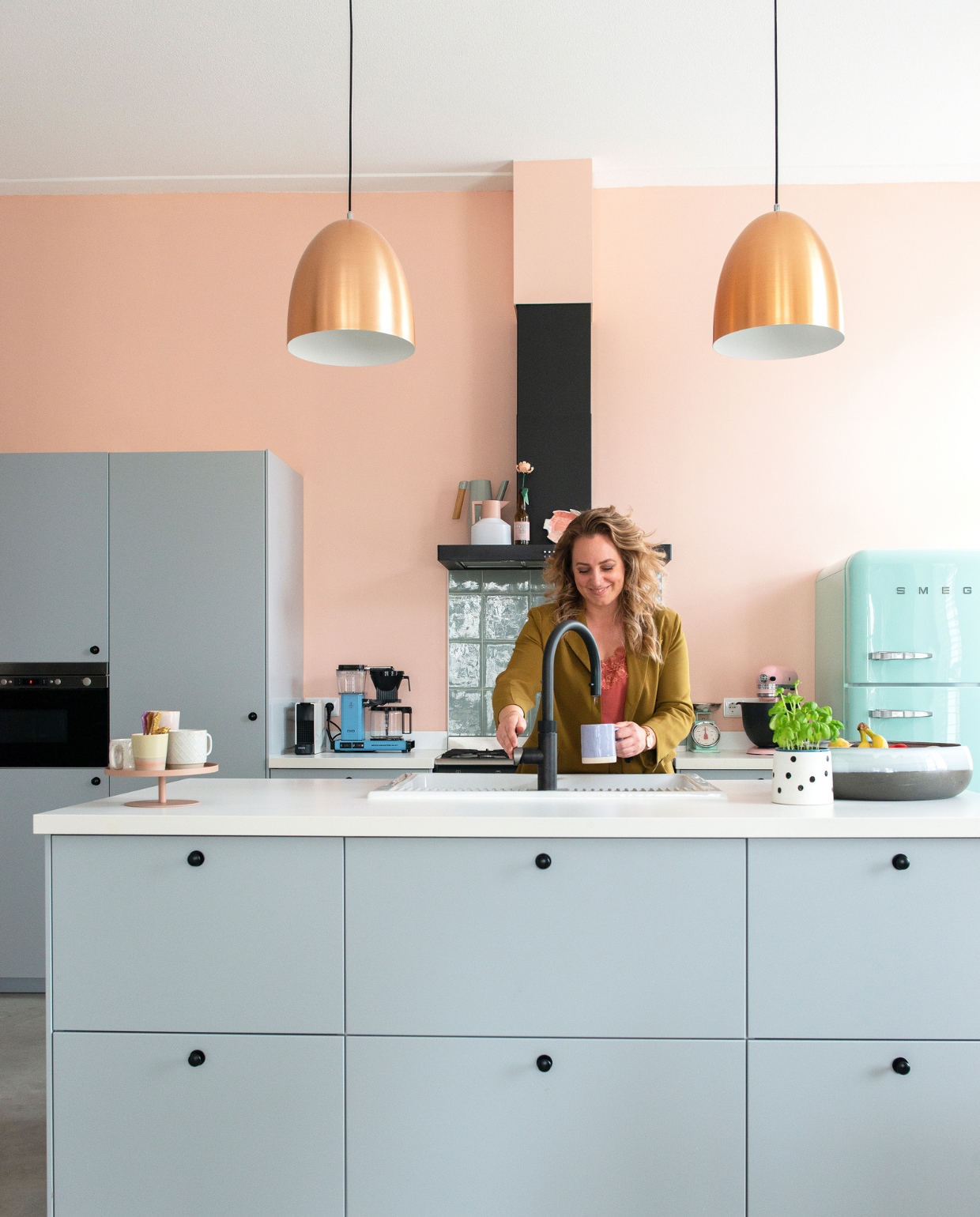 Keuken Metod met fronten Veddinge en gieter Ikea. Kraan Quooker. Koelkast en afzuigkap Smeg. Tegels vtwonen. Hanglampen Karwei. Koffiezetapparaat Moccamaster. Weegschaal Bloomingville. Mixer Kitchenaid. Taartplateau Designbite. Gespikkelde mok en lila mok Xenos, mok rechts Kwantum. Geel-roze mok en fruitschaal HKliving. Lepeltjes Sabre Paris. Bloempot Søstrene Grene. Thermoskan Normann Copenhagen. Flesje Mannenbier van Hema. Bloem Lego. Vissenbord &amp;klevering. Muurverf Chrysant van Flexa. Betonvloer. Overig onbekend. vtwonen 08-2022 | productie De Binnenkijkers | styling Jeske Weel | fotografie Caroline Coehorst