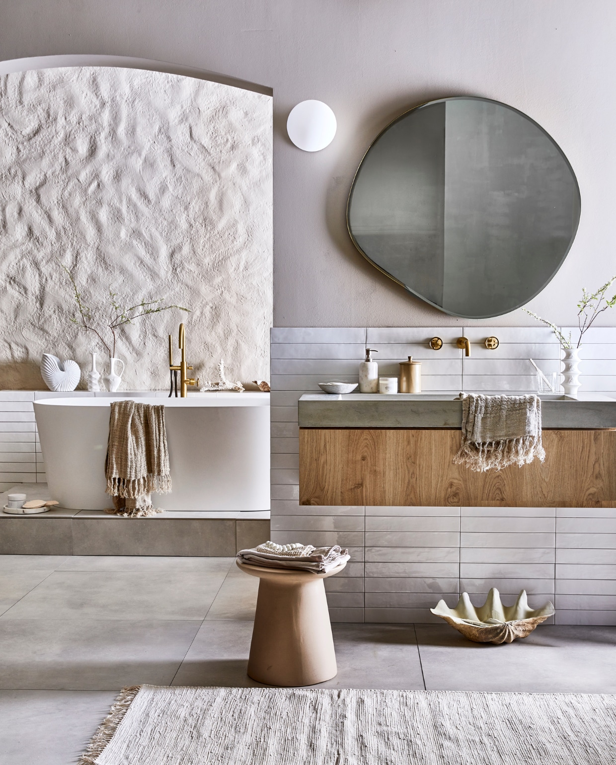 vtwonen collectie: Vloertegel Mold XL Cement, 90x90 cm. Wandtegel achter wastafel Marrakesh, kleur Nieve, glans, 6,5x40 cm (lxb). Wastafel Tank, beton, kleur Concrete, 10x120x46 cm (hxbxd). Onderbouwkast Cube, eikenhoutfineer, kleur Oak, 30x120x43,5 cm (hxbxd). Wandkraan Flame, kleur Bronze, inbouwdeel. Bad Tub. Badmengkraan Flame, kleur Bronze, vrijstaand. M.m.v. vtwonen.nl (muurverf kleur Flax, spiegel Ferm Living, wafelhanddoek Marc O’Polo), hkliving.nl (kruk, kleine witte vazen), nordal.eu (grote schelp, schelpvormige vaas, linnen badlakens, marmeren zeepdispenser), weldaad.com (marmeren schaaltje), hm.com (loper, grote marmeren schaal op vloer). De achterwand kreeg stuc effectief in kleur Flax van vtwonen (gemaakt door setbouw Milo Kol). vtwonen 08-2021 | productie Tanja Saarberg | styling Cleo Scheulderman | fotografie Jeroen van der Spek