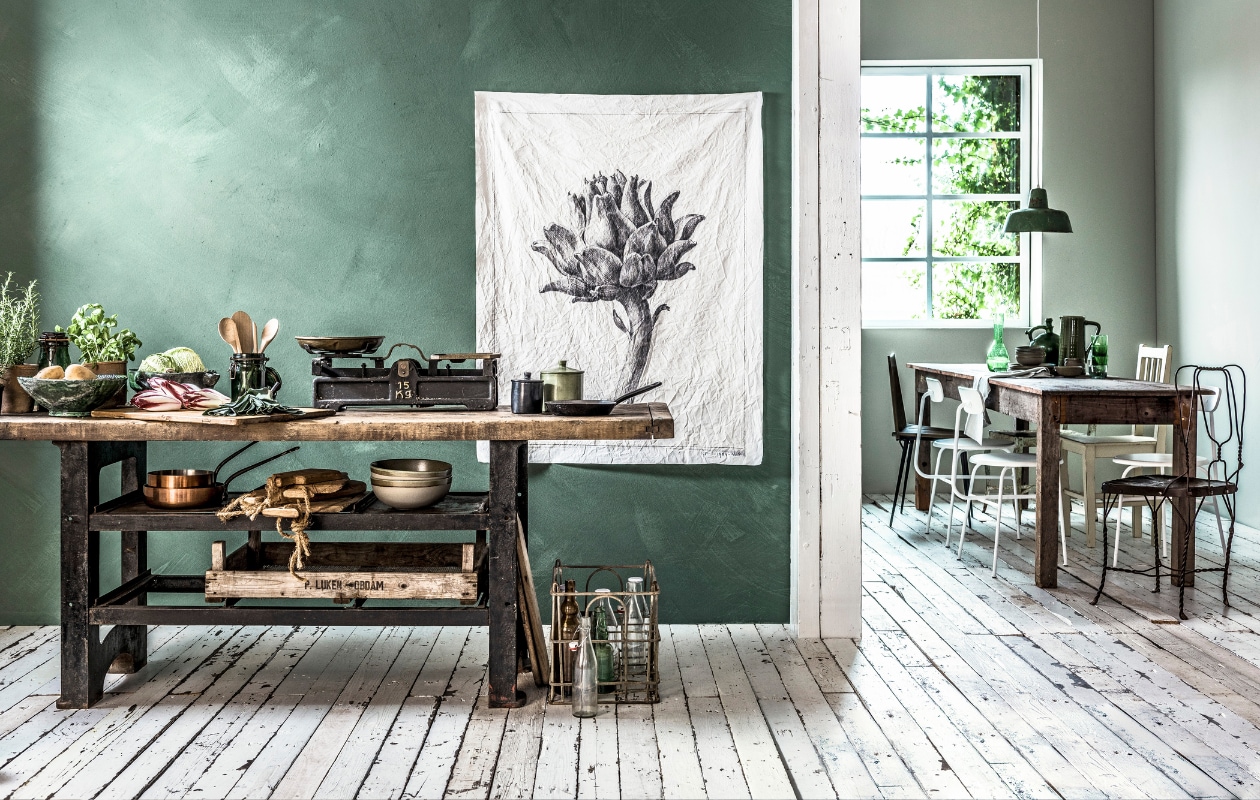 Muurverf in kleur Woodbine van Bauwerk Colour (We Are Wow Makers). Werkbank (Brût Amsterdam). Terracotta potten, groen glazen voorraadpotten, houten bak, beugelfles (De Weldaad). Groene schalen van keramiek (Eland&amp;vanderHelst). Houten pollepels en tang, schalen met rand (Nijhof). Weegschaal, koperen pannen (Neef Louis). Steelpan, krat, flessen (Van Dijk &amp; Ko). Zwarte pot van keramiek, groene pot van keramiek (MaisonNL). Grillig gevormde tapasplanken met touw (Raw Materials). Canvas poster bedrukt met afbeelding van Rijks Studio, groot formaat (www.rijksmuseum.nl, www.mo-ca.nl). In de eethoek: muurverf op de achter- en zijwand in kleur Rock van vtwonen (www.vtwonen.nl/vtwonen-collectie). Antieke hardhouten eettafel (Burbri Antiek). Witte metalen stoelen (Berden by Houweling). Houten stoel op zwarte metalen pootjes (Stadspaviljoen Noord). Lichtgroene metalen vintage stoel, groene glazen waterkan, groene glazen (Raw Materials). Oude houten stoel (Van Dijk &amp; Ko). Bruine metalen draadstoel (Eland&amp;vanderHelst). Groene metalen hanglamp (Neef Louis). Groen servies, groene hoge kan (Nijhof). Groene bolle kan (De Weldaad). Theedoek (Loods 5). vtwonen 08-2017 | styling Danielle Verheul | fotografie Sjoerd Eickmans