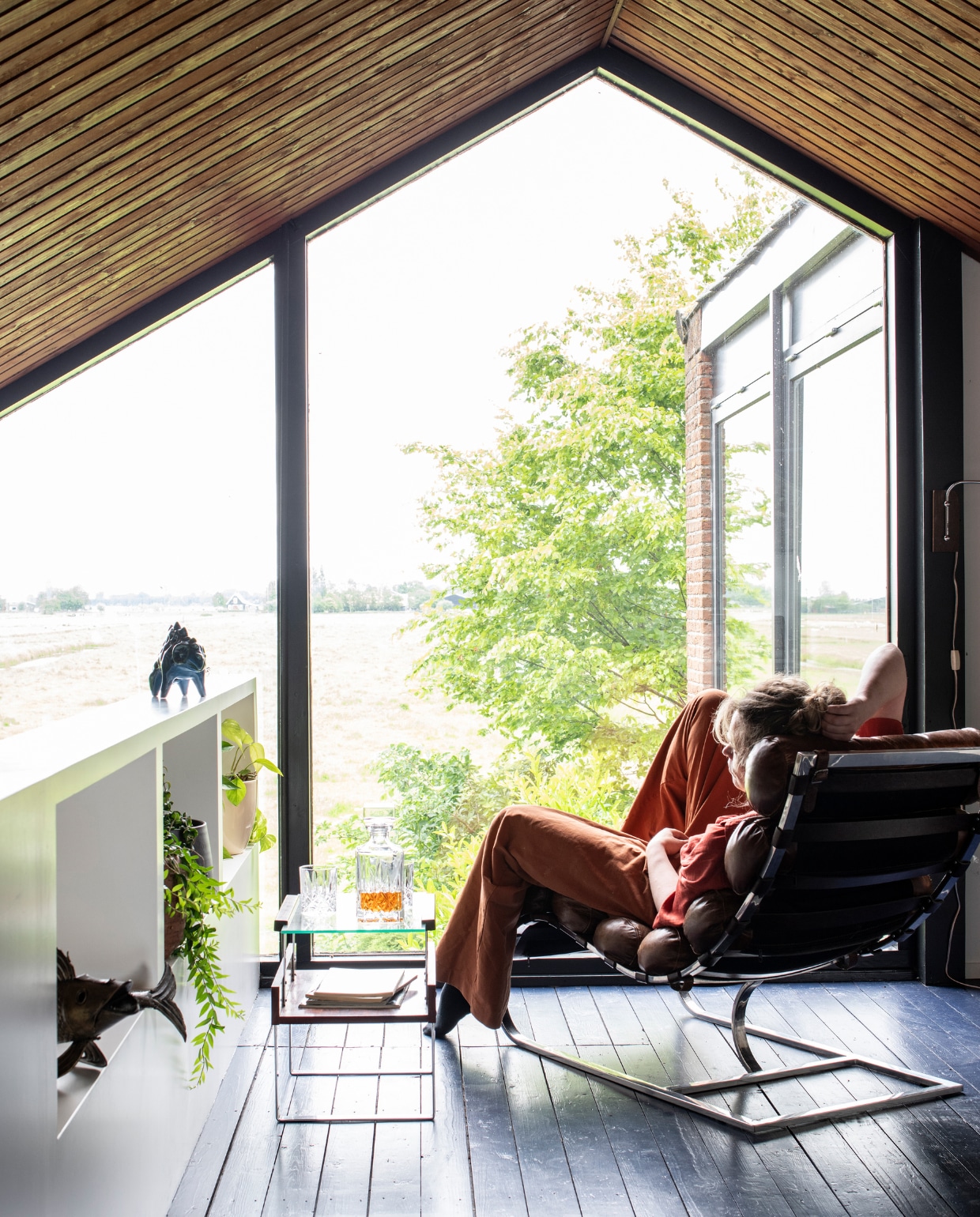 Relaxplek op de mezzanine. De oorspronkelijke houten vloer is gebeitst in een donkere tint (De Ru Amsterdam). Lounge stoel barbmama.nl, butler tray van euvintage.com, de blauwe vis was een huwelijkscadeau, fles en glazen van Nachtmann via de Bijenkorf. vtwonen 01-2020 | styling Kim Timmerman/Insidehomepage | fotografie Louis Lemaire