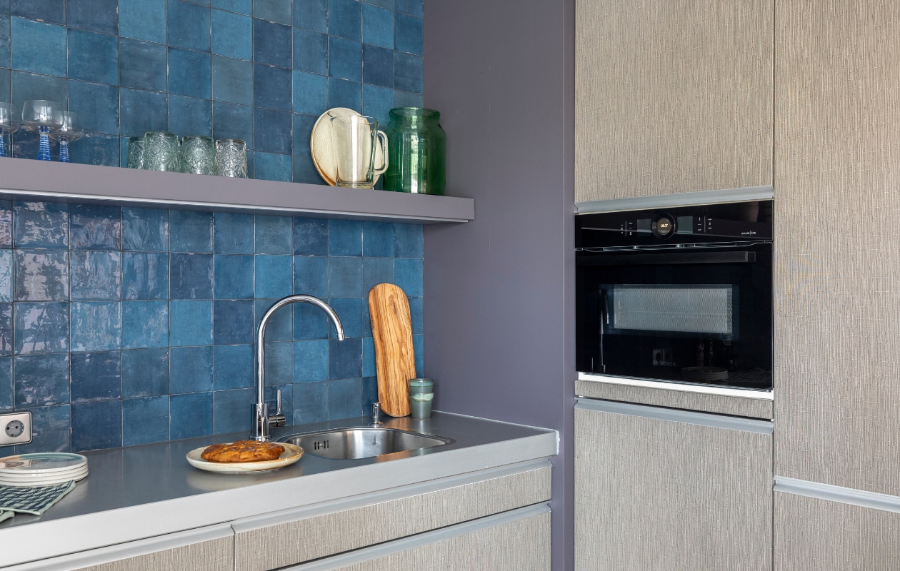 Flexa Creations muurverf Dark Tulip, op de kast Violet Whiff (flexa.nl). Op maat gemaakte kast (remmers-design.nl). Ladesystemen (vanhoecke.be). Keuken gewrapt in nummer T10 van Coverstyl (keukentrend.com). Wandtegels vtwonen tegels by Douglas &amp; Jones Craft Midnight Blue glossy, 12,5x12,5 cm (douglasjones.nl). oven CMG836NC1 (bosch-home.nl). Snijplank in de kast van Bowls and Dishes, krat van Hay, kopjes van HKliving, wijnglazen van HKliving, dinerborden van HKliving, ontbijtborden van HKliving, houten plank van Bowls and Dishes, theedoeken van Hay (vtwonen.nl). Olijfolie- en azijnset, olijfolie, 250 ml, olijfolieblik (bowls-dishes.com). Kunstwerk in de kast Zonsopgang van Jacob von Sternberg Art (werkaandemuur.nl). Weer verliefd op je huis seizoen 17 aflevering 3 | styling Marianne Luning | fotografie Margriet Hoekstra