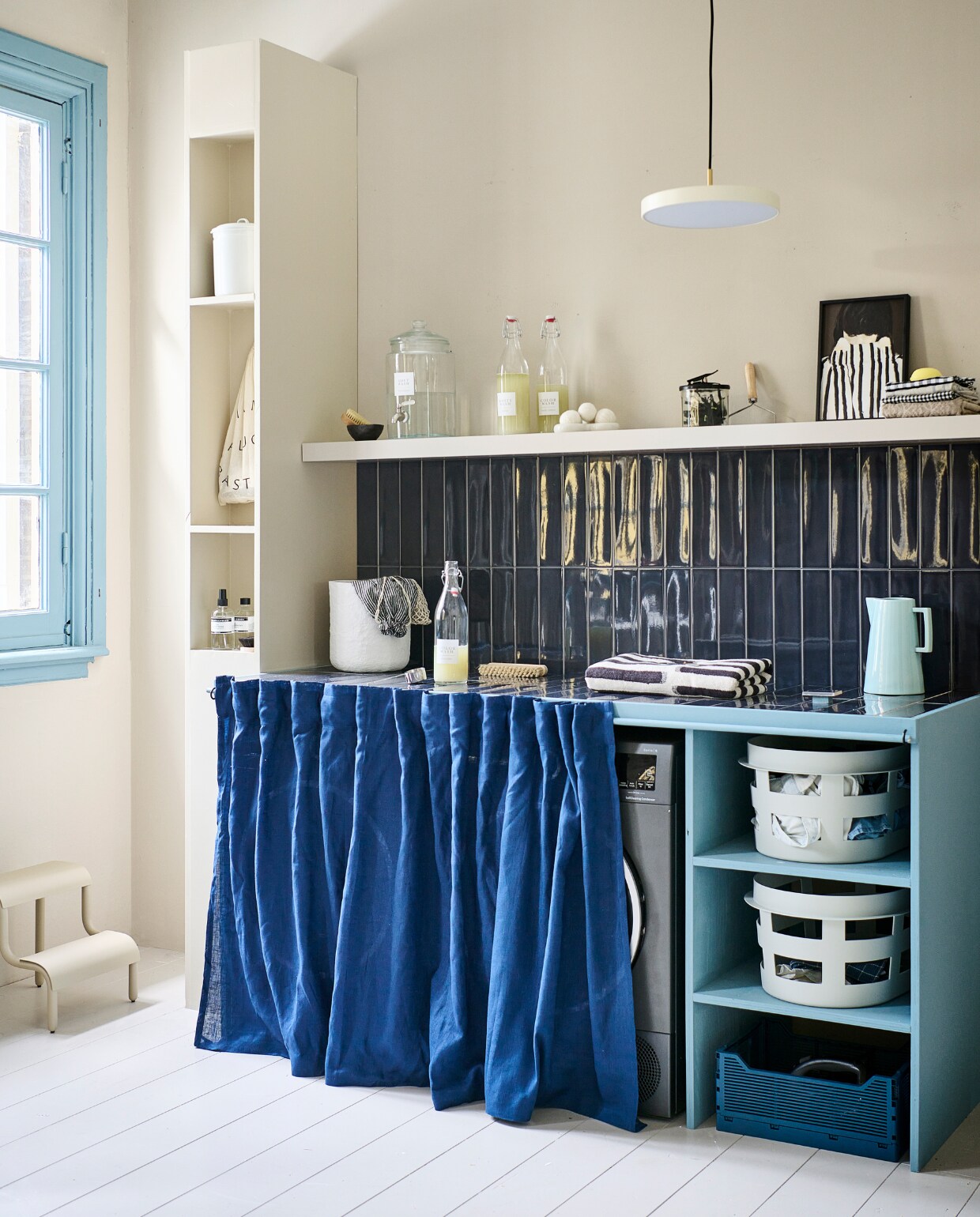 Lakverf wasbar Old Blue van vtwonen, 500 ml € 20,99, muurverf Warm White van vtwonen, 1 liter € 27,99 (karwei.nl). Lakverf kozijn Wit Golven, 500 ml € 30,99 (flexa.nl). Tegels Shapes van vtwonen in Titanium Blue Glans, 30x7,5 cm, per m2 € 59 (go.vtwonen.nl/collectie)  Lamp Asteria van Umage € 179,45, kunststof wasmand van Hay € 39,-, metalen kruk van Ferm Living € 139, katoenen handdoek van HKliving € 49, katoenen mand van Ferm Living, set van 3 € 269,- (vtwonen.nl/shop). Emaillen blik € 9,95 (dille-kamille.nl). Wasmachine € 1069, warmtepompdroger € 1149 (bosch-home.nl). Houten plank Lack € 29,99 (ikea.nl). Print Shy € 35,- (mydeerartshop.nl). Aardewerken kan Dik € 39,- (hollanddesignandgifts.com). Flessen linksonder in kast vanaf € 19,50 (marie-stella-maris.com). Flessen wasmiddel, pag. 44. Kleed Lohals, € 72,95 (ikea.nl), pag 34.Overig privébezit. vtwonen special DIY 8-2023 | styling Kelly van Gendt, Corrien Flohil | uitvoering Erik de Jong | fotografie Sjoerd Eickmans
