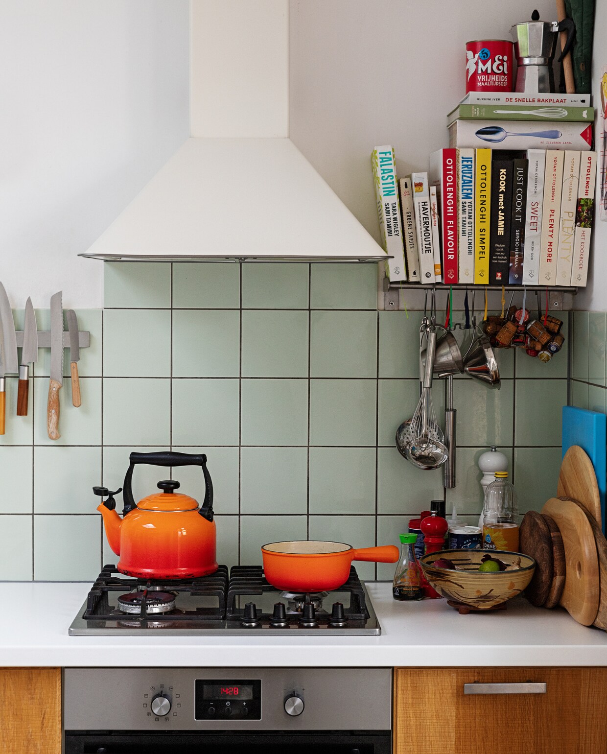 Oranje fluitketel en pan Le Creuset. Messen Suncraft, Opinel en Dille &amp; Kamille. Kookboeken Ottolenghi, Jamie Oliver, Sergio Herman, Yvestown in de keuken, De Zilveren Lepel. Snijplanken Hay, Ikea en Serax. Peper- en zoutmolen Peugeot. Soeplepel Brabantia. Hangend rvs keukengerei Dille &amp; Kamille. Percolator tweedehands. Schaaltje van een pottenbakkersmarkt. Afzuigkap en oven Ikea. Ovenhandschoen Kook. Pollepel Kookhuis aan de Maes. vtwonen 13-2021 | styling Ilona Jongepier | fotografie Dana van Leeuwen