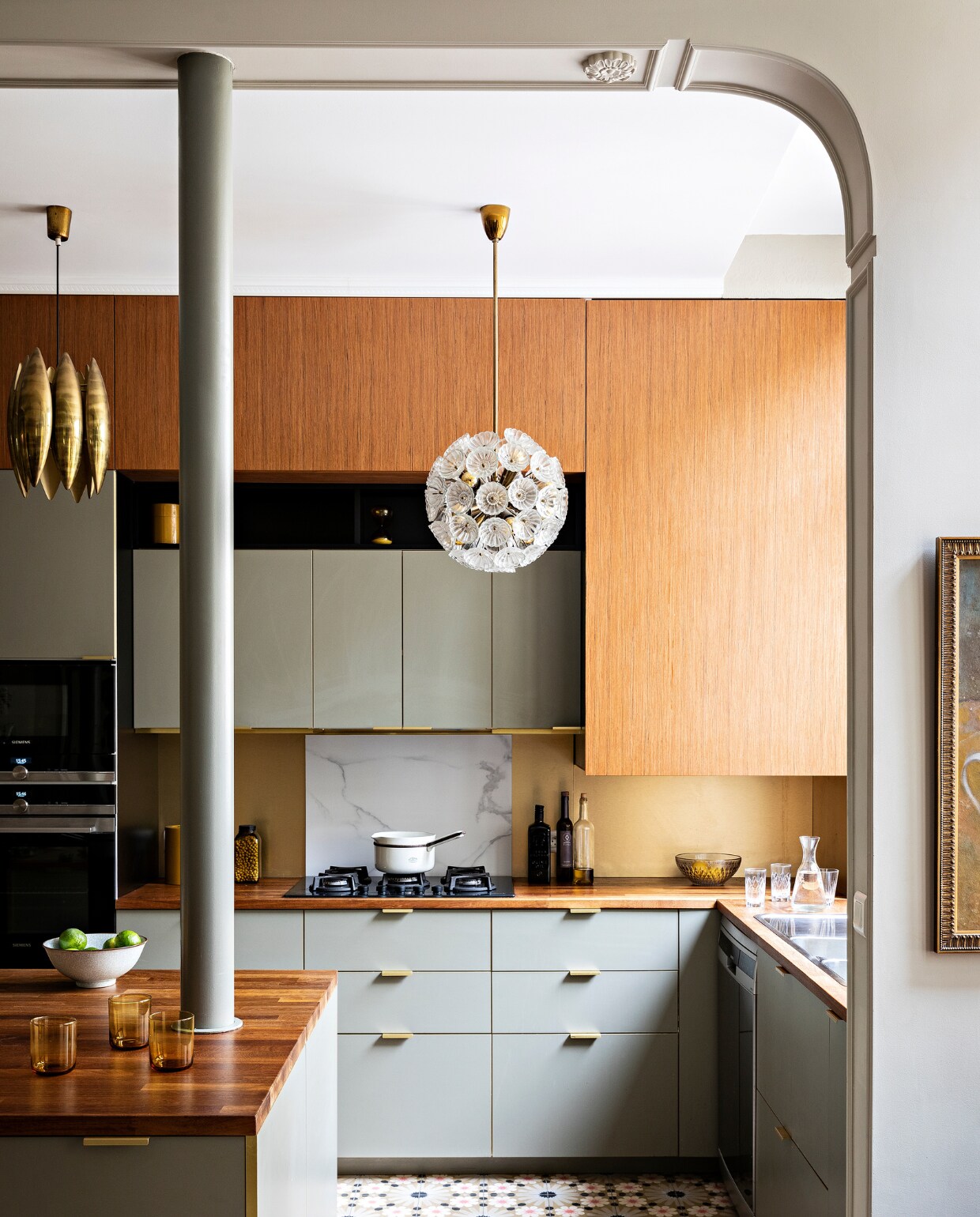 Basiskeuken Ikea, deurtjes en grepen Bocklip, teakhouten werkblad Ixana, teakhouten bovenkasten Dispano. Messing Florence Knoll-hanglamp en glazen Emil Stejnar-hanglamp   vintage. Overig onbekend. vtwonen special binnenkijken 03-2022 | productie AC Scoffoni | styling Marie-Maud Levron | fotografie Yann Deret