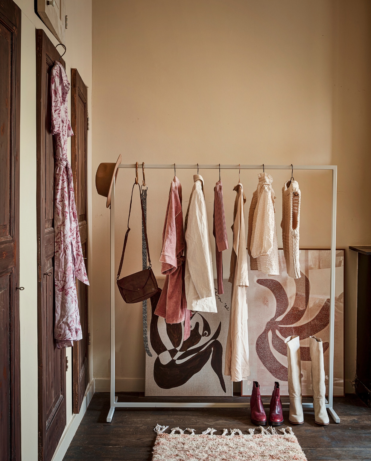 Gebloemde jurk aan deur € 99,99, leren tas € 34,99, riem € 32,50, gebroken wit colbert € 99,95, lange jurk € 89,95 (mensinkmode.nl). Wollen hoed € 34,95, bordeauxrode enkellaarzen € 69,- (@flowerchild.arnhem). Kledingrek Julie in RAL 7044, 140x157 cm € 299,18 (fashionracks.nl). Bamboe s-haken per stuk € 3,50, gebroken witte smock top € 69,99, gebreide waistcoat € 99,95 (loftloft.nl). Velours badjas € 150,- (@studio.cherrymoon). Oudroze shirt met streep € 39,95, hoge laarzen € 129,95 (@sparqelle). Kunstwerk No.22 Engelen, 60x80 cm € 485,- (sifravieten.com). Handgemaakte print Let’s Go Bananas, 70x100 cm € 249,- (enkelartstudio.com). Berber vloerkleed, 77x178 cm € 275,- (thesouks.nl). vtwonen 10-2022 | styling Demelza Krens | fotografie Peggy Janssen