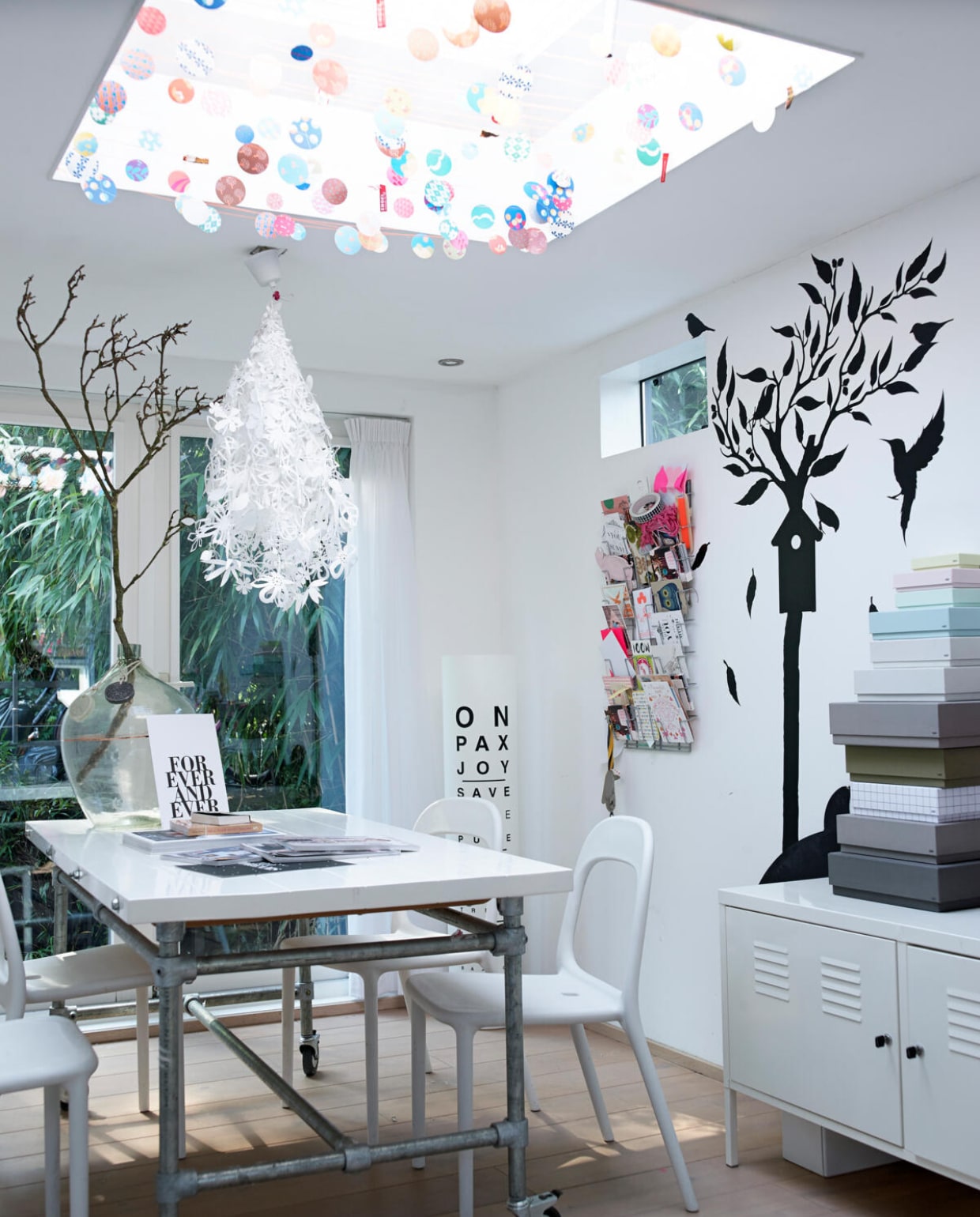 De happy-werkkamer van Natascha. De werktafel is een ideale brainstormplek en zelfgemaakt van Kee Klamp buizen (Nijhoff), witte planken en wielen. Lamp: Tord Boontje. Kleurrijke slinger bij de lichtkoepel: Engel. Muursticker: Kek Amsterdam. De lamp kocht ze jaren geleden bij Ligne Roset. Lockerkastje en stoelen van Ikea. Natascha kreeg de vaas cadeau van vrienden. ‘Die komt uit Frankrijk en werd daar vroeger gebruikt om wijn in te vervoeren.’ Postertje For Ever and Ever van The Birds and the Bees via Flavouritesstore.nl  vtwonen 07-2014 | fotografie Tjitske van Leeuwen | styling Marianne Luning