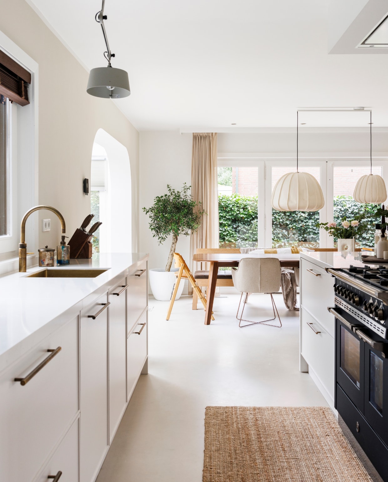 Gietvloer Arturo, muurverf keuken Sandy Beach van Flexa, verf overige wanden Ral 9016. Op maat gemaakte keuken Keukenstudio Stormink. Oven en fornuis Steel. Plafondafzuigkap Novy, jaloezieën Topjaloezieën, gordijnen Karwei, grijze hanglamp Tonone, beige hanglampen Ay Illuminate. Olijfboom en bloempot Intratuin. Kinderstoel Kaos, eettafel De Machinekamer, stoelen Jesper Home, loper Ikea, messenblok Rösle, potje Ferm Living, zeeppomp Jotex, kraan Quooker. Overig onbekend vtwonen 03-2024 | fotografie Margriet Hoekstra