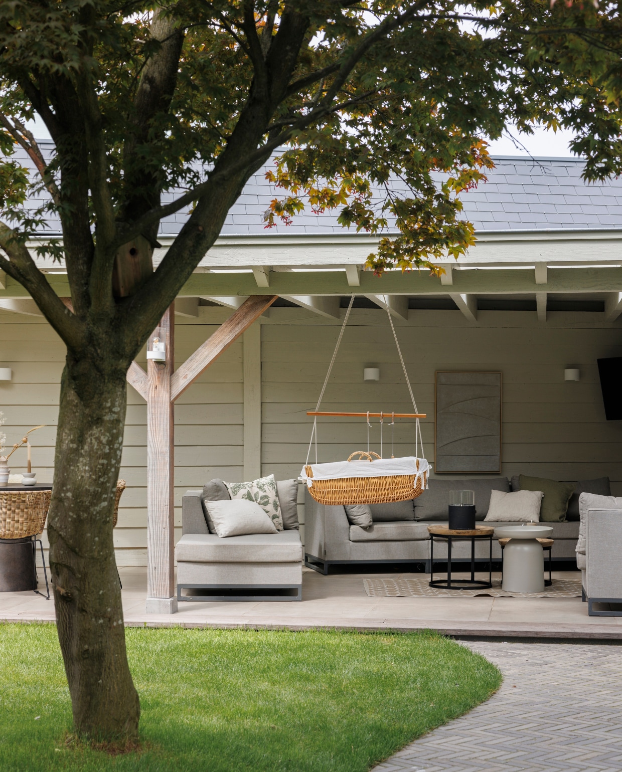 Pergola Janse &amp; Berkhof Tuinen, verf pergola Shadow White van Farrow &amp; Ball, tuintegels Vida waalformaat, tegels onder pergola GeoCeramica, hangwieg erfstuk, loungeset Exotan. Salontafels en wanddecoratie By-Boo. Tafelhaard Cosi Fires, wandlampen Rietveld Licht, televisie Philips. vtwonen 03-2024 | fotografie Margriet Hoekstra