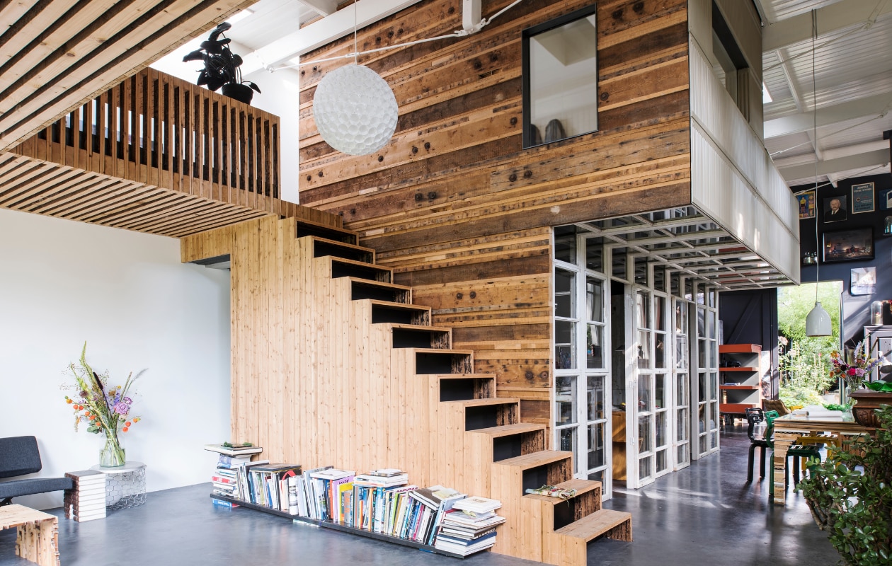 Boven zit de slaapkamer van Rolf en Yffi, daaronder de keuken. Links loop je naar hun walk-in closet. Naast de trap liggen designboeken en tijdschriften. De plant op de eerste verdieping is van vilt en gemaakt door Wandschappen. De witte lamp van plastic bekers is gemaakt door Rolf, maar dit is een bestaand idee. De zwarte bank is van Mart Visser voor Spectrum. Naast de bank staat de Princely Stool, ontworpen door Rolf. Het tafeltje is van Xeen. Mand gekocht in Cambodja. Voor de bank staat een houten salontafel genaamd Slices of Henry Deux, die is ontworpen door Rolf. De wand is opgebouwd uit delen van spanten en de trap met dakbeschot.