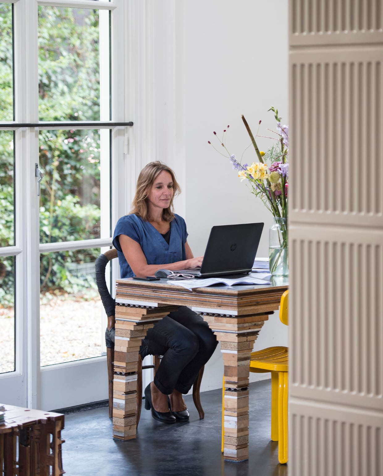 Yffi aan het werk aan de tafel die gemaakt is van oude materialen uit de barak. Rolf ontwerpt en maakt de tafels met de naam Tafel van het huis op aanvraag uit materiaal dat vrijkomt bij een verbouwing. Gele Chubby Chair van Dirk FMannin. vtwonen 03-2017 | styling Inge van Lieshout | fotografie Louis Lemaire/Insidehomepage