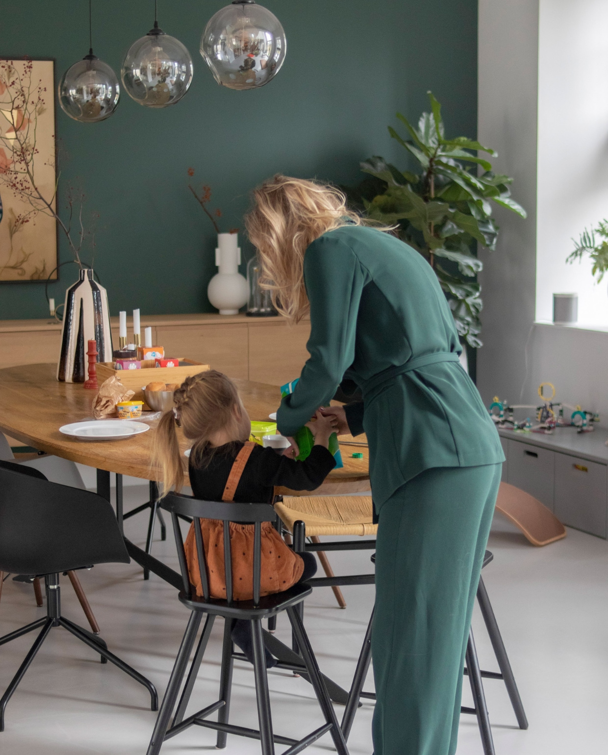 Muurverf Frivool van Histor, tafelblad Marktplaats met onderstel gemaakt door Vitriwand, rieten stoelen en boekenstandaard Loods 5, kinderstoelen Ikea, kuipstoelen Mobelaris, kunstwerk Chris Luka, hanglampen Wonenmetlef, tafellamp zelf samengesteld, dressoir gemaakt door Mh Design Meubelen, kaarsen en vaas op tafel Zara Home, witte vaas HKliving, balansbord Wobbel, kist vtwonen. Overig onbekend. vtwonen 11-2022 | productie CocoFeatures | fotografie Anne de Haan