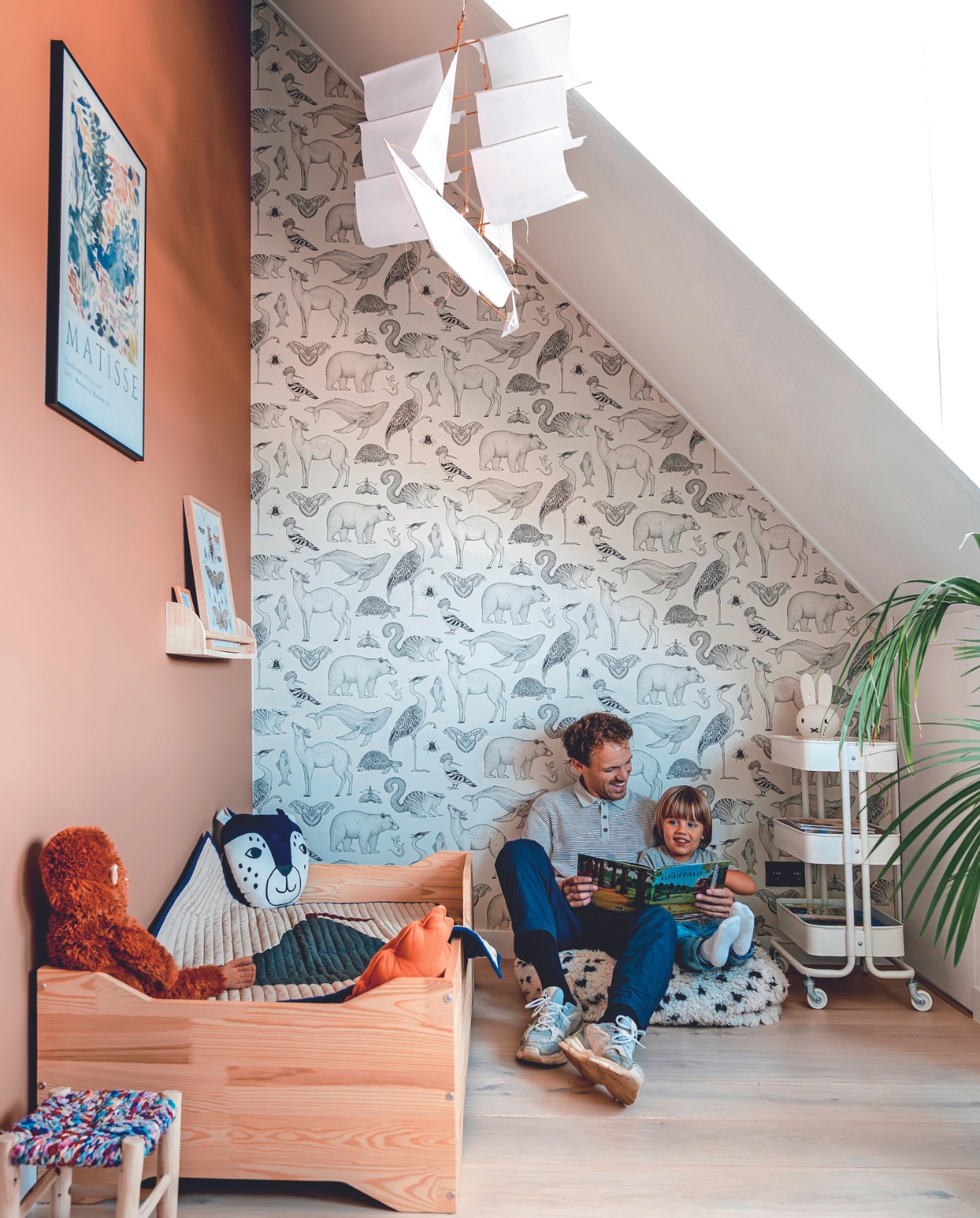 Muurkleur Dandy Dust van Flexa, behang Ferm Living, eiken parketvloer Multiplank van Laminaat en Parket, lijst Desenio, poster Matisse, boekenplank Zara Home, lijst erop Postery, kruk Le Petit Nomade, kinderbed Petit Puk, beddengoed Crisp Sheets, sprei Ferm Living. Aap en trolley Ikea. Knuffelkussen Nobodinoz, kussen oranje blad H&amp;M Home, zeilschip Haptic Lab via Ziloen, poef Studio Pure, lamp Nijntje Mr Maria, plant Kentiapalm. Overig onbekend. vtwonen 02-2024 | fotografie Myrthe Slootjes | tekst Mirjam Rosema-Verhulst