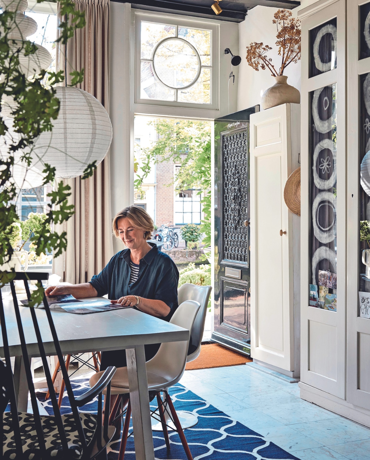 vtwonen 02-2024 BK3: Vloerkleed Ikea, tafel DIY van vtwonen van ontwerper Frans Bramlage. Stoelen Vitra en erfstuk. Papieren lampen Ikea en Chinese winkel. Blauwe doeken kast en witte vaas zelfgemaakt door Heleen. Gordijnen Hema. Marmeren vloertegels origineel, servieskast al jaren oud. Verfkleur plafond Royal Blue van Flexa. Overig onbekend. vtwonen 02-2024 | fotografie Alexander van Berge
