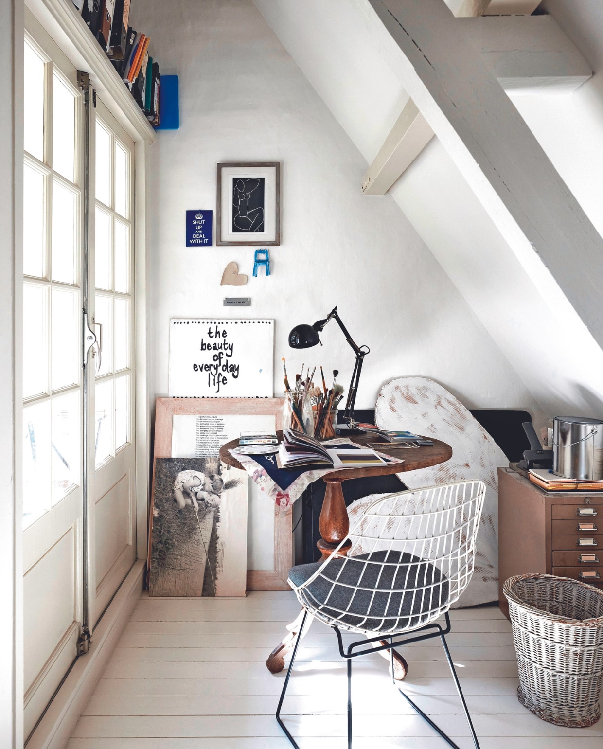 vtwonen 02-2024 BK3 - Draadstoel, archiefkast en witte mand erfstukken. Tafel &amp;Klevering. Bureaulamp Ikea, print Matisse uit jaarkalender, kartonnen stoel aan wand Klaas Gubbels. Hartje en spreuk op wit canvas gemaakt door Heleen. Ingelijste tekst van een beurs in Londen, oude jeugdfoto. Het vtwonen-hart uitgevoerd in karton, ontworpen en gemaakt door Heleen. Verf vloer, muur en balken Ral 9010 van Flexa. Overig onbekend. vtwonen 02-2024 | fotografie Alexander van Berge