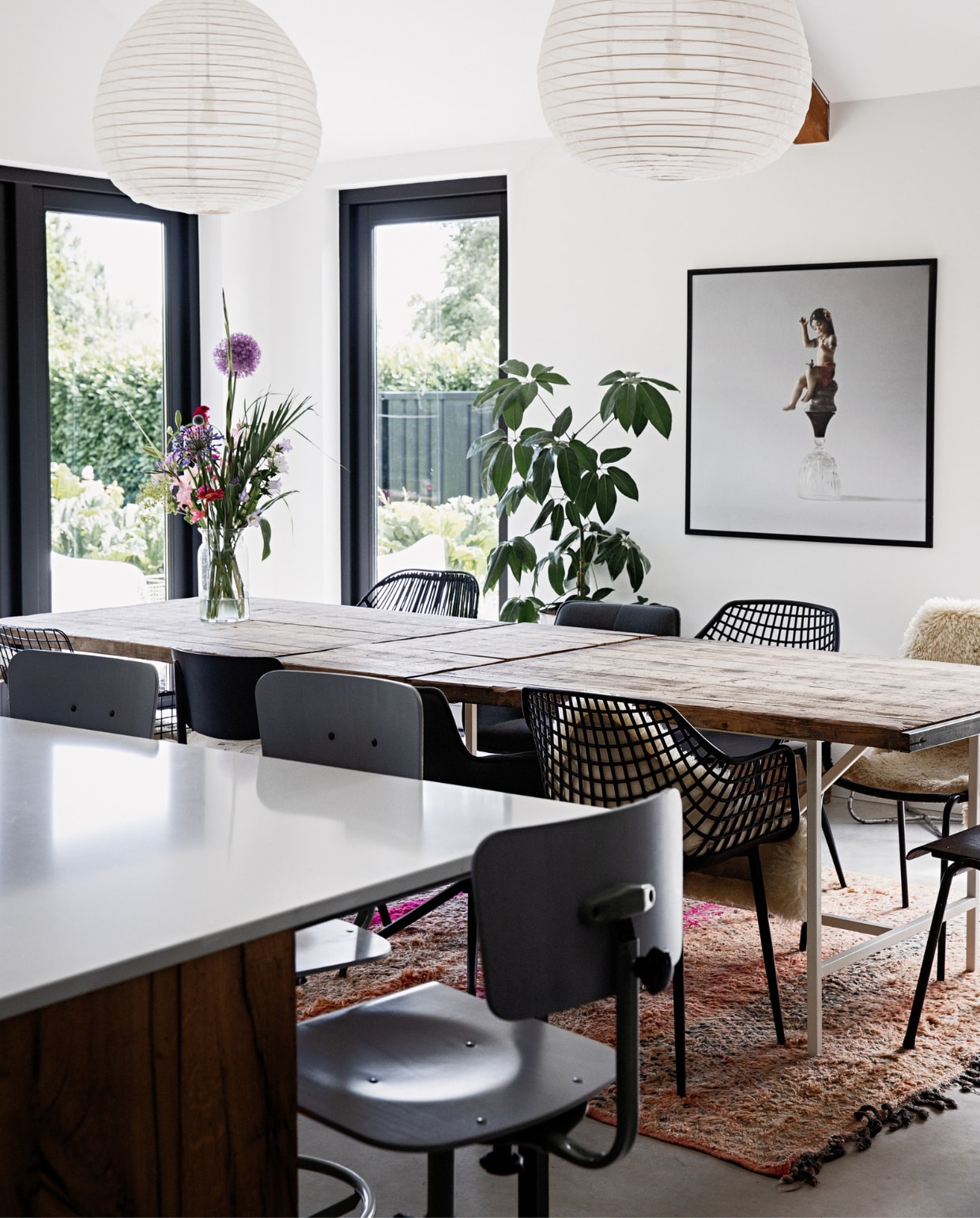 Muurkleur Ral 9016, kleur kozijnen Ral 9005, vloer gevlinderd beton van Bull beton, aanrechtblad De Keukenbladenfabriek, barstoelen De Machinekamer, tafel oude steenschotten op een op maat gemaakte stalen onderstel Gillissen Ontwerp. Stoelen (v.l.n.r. deze kant) draadstoel HKliving, schoolstoel Burbri Antiek, kuipstoel Kwantum, stoffen draaistoel Loods 5, (v.l.n.r. andere kant) zwarte rotan stoel en stoffen draaistoel Loods 5, kuipstoel Kwantum, schoolstoel Burbri met schapenvacht Ikea. Plant gekregen, glazen vaas Bloomon, foto Sake Elzinga, kleed handgemaakt Loods 5. Hanglampen onbekend. vtwonen 12-2022 | styling Ilona Jongepier | fotografie Dana van Leeuwen