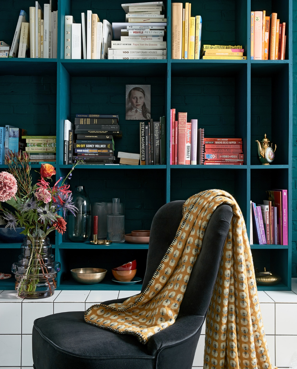 Boekenkast in kleur Marina Blue matte lak € 45,- per liter (Little Green). Fluwelen stoeltje Remsta € 149,- (ikea.nl). Plaid Klara € 79,- (made.com). Rood kommetje € 2,99, mat gouden theepot € 9,99 (xenos.nl). Grijze glazen vaas Ruby grey € 19,99 (casashops.com). Geribbelde vaas Hilmir € 12,99, vaas Manfred € 9,99 (jysk.nl). Kunstbloemen v.a. € 2,95 (casashops.com). Foto vrouw, prijs op aanvraag (racheldubbe.com). Overig privébezit. vtwonen 03-2020 | styling Fietje Bruijn | fotografie dennis brandsma