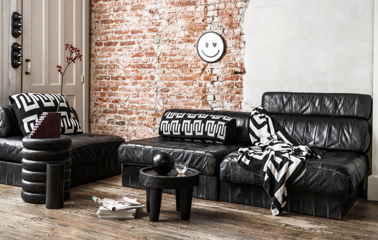 Zwart-wit rond kussen, gebreid bci-katoen, 20x50 cm € 49,95, zwart-witte plaid met verschillend dessin aan beide kanten, gebreid bci-katoen, 130x170 cm € 99,95, zwarte metalen vaas, 20x20 cm (Øxh) € 34,95 vtwonen.nl/shop. Overig privébezit. vtwonen 10-2023 | productie &amp; styling Tanja Saarberg | fotografie Stan Koolen