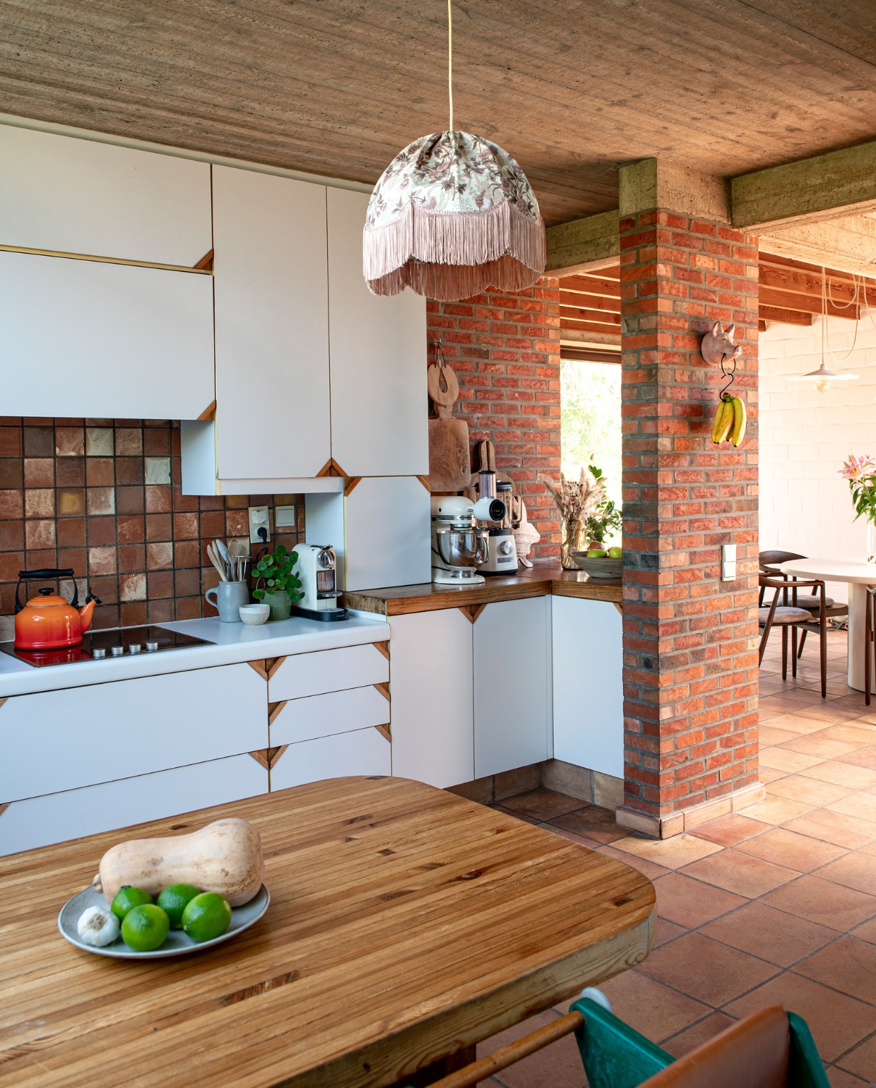 Fluitketel Le Creuset. Fruitschaal onbekend. Kinderstoel Hokus Pokus. Hanglamp kringloop. Keukenmachines Magimix en KitchenAid. Potten op het aanrecht kringloop. Varken aan de muur souvenir uit Frankrijk. Houten planken tweedehands. vtwonen 03-2023 | productie De Binnenkijkers | styling Jeske Weel | fotografie Caroline Coehorst