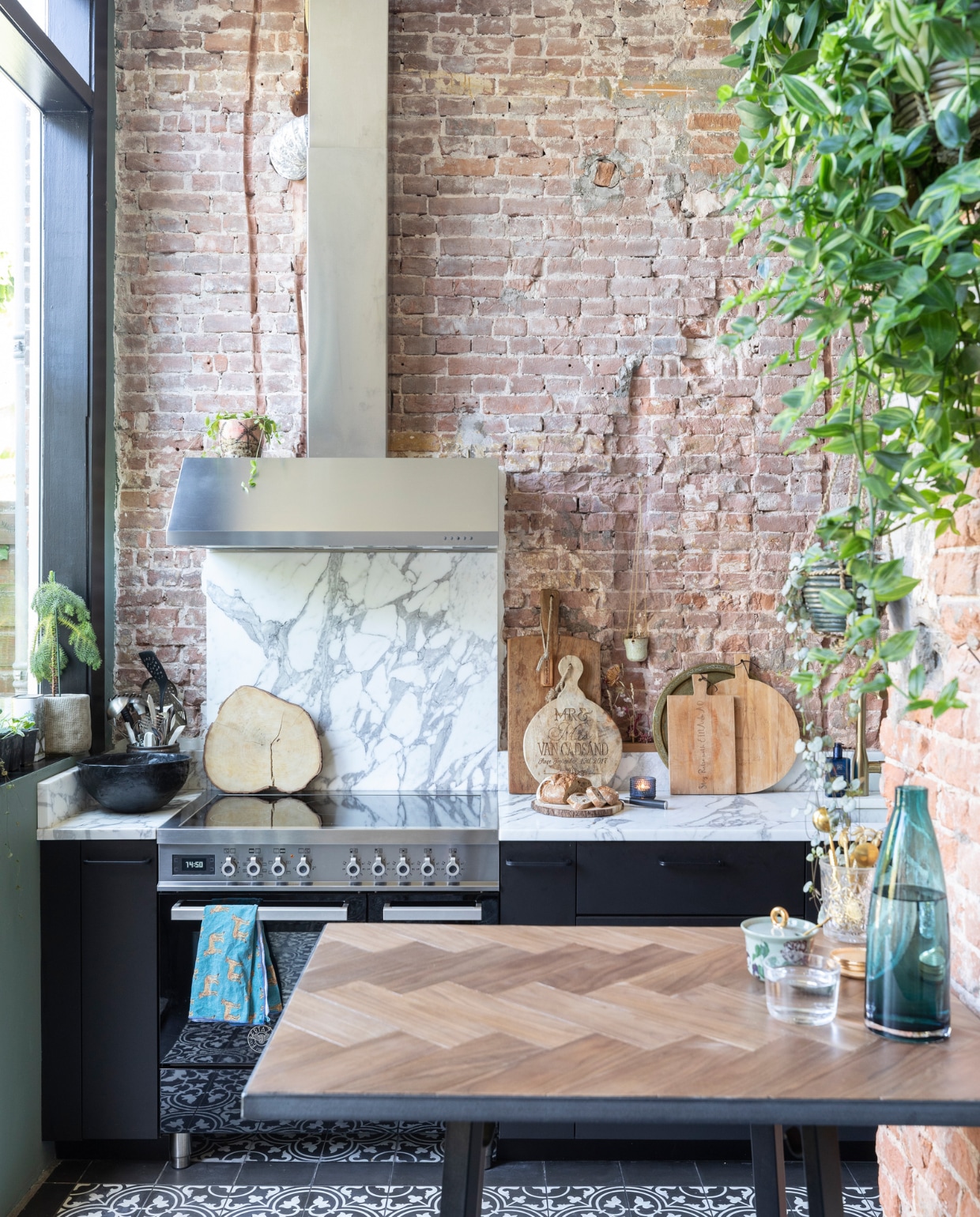Portugese vloertegels Designtegels, keukenkastjes Ikea, werkblad en spatwand van Carrara marmer door Swaalf uit Haarlem, fornuis Bertazzoni, groene muurverf Green Smoke en zwarte verf kozijnen Pitch Black Farrow &amp; Ball, pot in vensterbank, blauwe waterkan, waterglas en zwarte schaal Ikea, snijplank boomstam laten maken op Bali, snijplanken gekregen van vrienden, hangpot Dekatuin, pot op afzuigkap gekregen, hoge bartafel onderstel van Hay met massief eikenhouten blad gemaakt door SkillsXL, suikerpot van Essenza, vaas onbekend. vtwonen 01-2021 | productie en fotografie Margriet Hoekstra