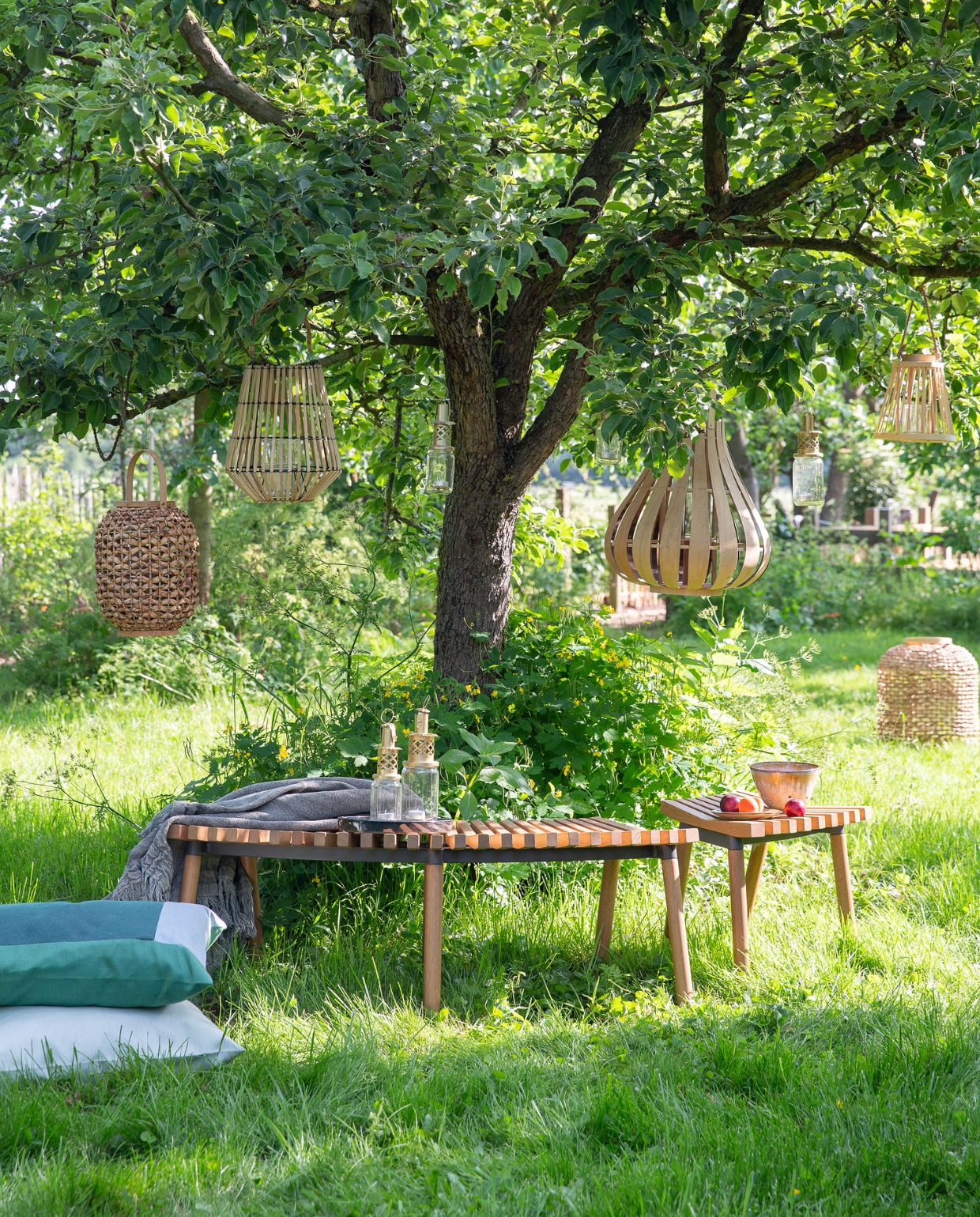 Bank Överallt, 124x49x44 cm (bxdxh), kruk Överallt (ikea.nl). Lantaarns van links naar rechts in de boom: XL van gevlochten gras en jute (deens.nl), van bamboe (action.com), jampot maat M (householdhardware.nl), van bamboe met glas erin van Pols Potten, 45x48 cm (vtwonen.nl), jampot maat M (householdhardware.nl), taps toelopend van bamboe met glas erin (action.com). Lantaarn XXL van gevlochten gras en jute (deens.nl). Mintgroen duurzaam buitenkussen Solid, 60x60 cm, mintgroen buitenkussen Bengali (kus-sen.nl). Linnen plaid, 130x170 cm (aaimadewithlove.com). Lantaarns van gerecyclede jampotten (householdhardware.nl). Fruitschaal en schotel (lilokeramiek.nl). vtwonen 08-2019 | styling Leonie Mooren | fotografie Anouk de Kleermaeker