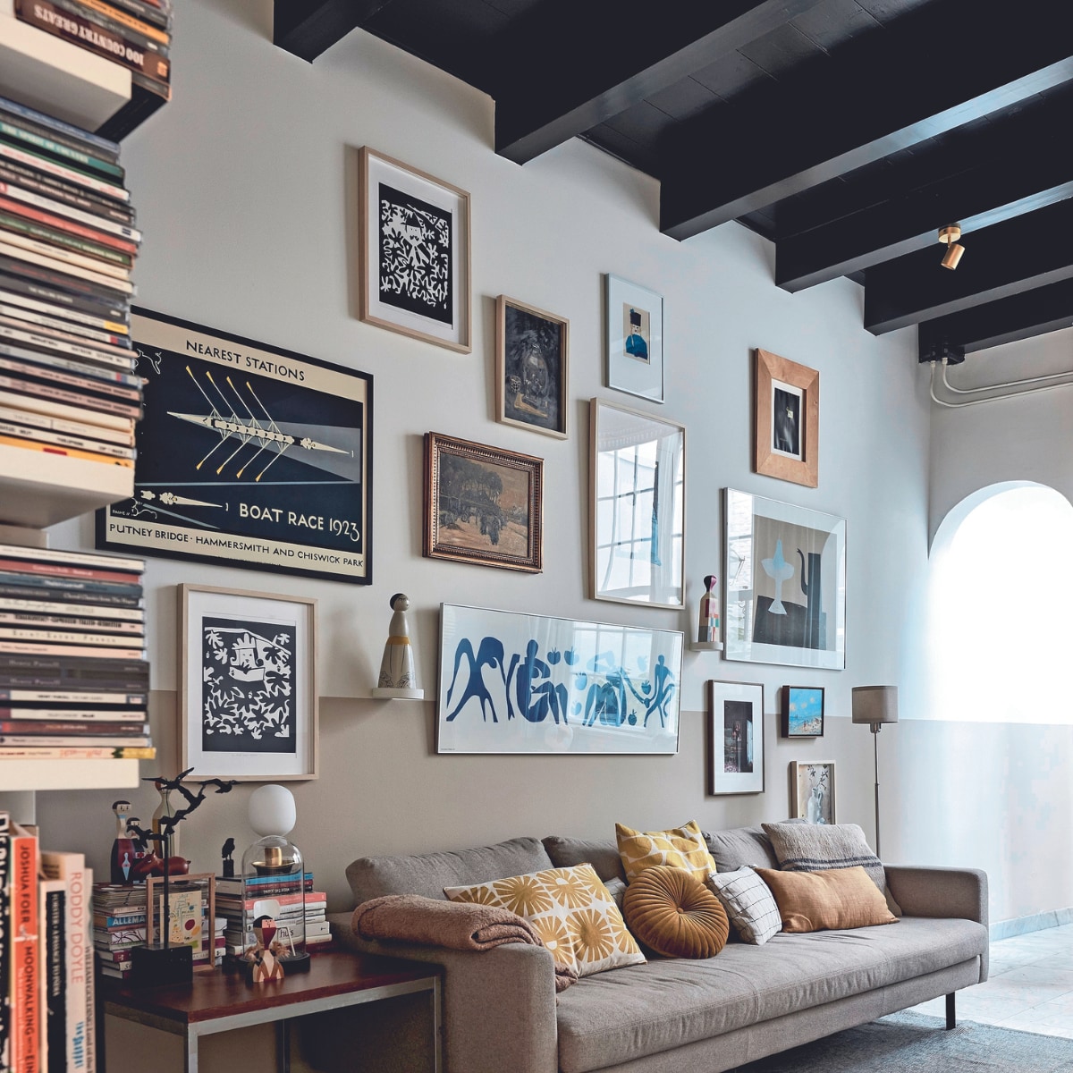 Bank Loods 5. Plaid, rond kussen en effen geel kussen Zara Home. Kussen met zonnetjes, geel-wit kussen, klein kunstwerk op bijzettafel cadeaus. Geblokt kussen zelfgemaakt van Habitat-stof, grijs kussen gemaakt met stof van de markt. Bijzettafel kringloop. Zwart kunstwerk vogels en kleine zwarte vogel familiestukken. Houten beeldjes en leren nijlpaard Vitra. Stolp met model van Revolt-stoel vintage. Tafellamp, vloerkleed en kap stalamp Ikea. Aan de muur: zwart-witte zeefdrukken, schilderij stilleven, persoon met zwarte hoed, groot rechthoekig wit werk in het midden en klein werk vaas met bloemen zelfgemaakt door Heleen. Boat Race 1923 en klein lichtblauw kunstwerk cadeaus. Zeefdruk theepot Klaas Gubbels, ingelijste poster Matisse Ikea, foto Frederique Masselink-van Rijn. Overige makers onbekend. Beeldje gekocht op Bali. Object Vitra. Muurverf  Ral 9010 van Sikkens. Verf lambrisering Pure Mild Sand en plafond Royal Blue van Flexa. Overig onbekend. vtwonen 02-2024 | fotografie Alexander van Berge