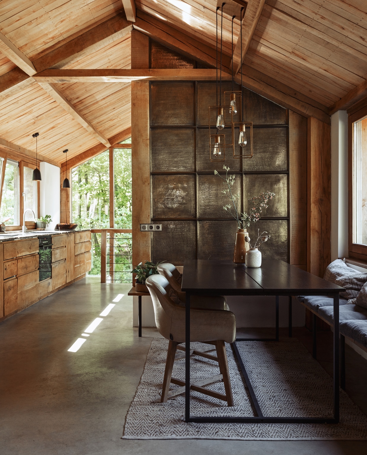 Vloer gevlinderd gegoten beton, kleed Goround Interior, eettafelstoelen Lifestyle Home Collection, eettafel van Woood via Gamma, lamp Light &amp; Living, witte vaas Villeroy &amp; Boch, gele vaas Hema, takken uit eigen tuin, keuken Ikea met op maat gemaakte fronten van eiken, wand beplakt met dienbladen van de groothandel. vtwonen 07-2022 | styling Ilona Jongepier | fotografie Dana van Leeuwen