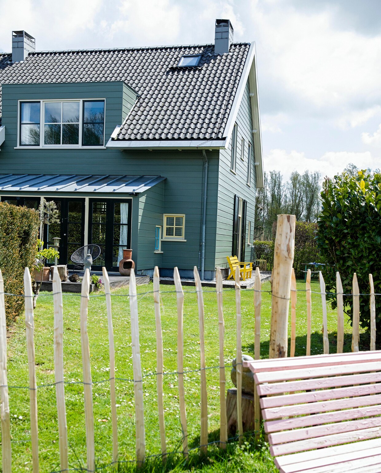 Het huis is aan de buitenkant afgetimmerd met hout, maar heeft een betonnen constructie. De kleur is bepaald door de monumentencommissie en mag niet worden veranderd. Tuinbank van de kringloop geschilderd in Nancy’s Blushes van Farrow &amp; Ball. vtwonen 07-2021 | styling Ilona Jongepier | fotografie Dana van Leeuwen