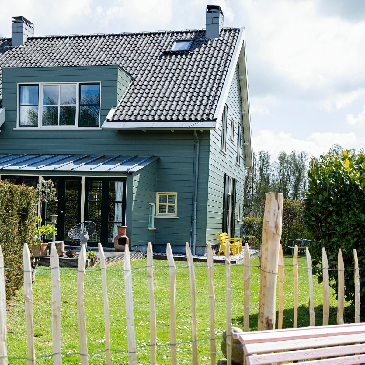 Het huis is aan de buitenkant afgetimmerd met hout, maar heeft een betonnen constructie. De kleur is bepaald door de monumentencommissie en mag niet worden veranderd. Tuinbank van de kringloop geschilderd in Nancy’s Blushes van Farrow &amp; Ball. vtwonen 07-2021 | styling Ilona Jongepier | fotografie Dana van Leeuwen
