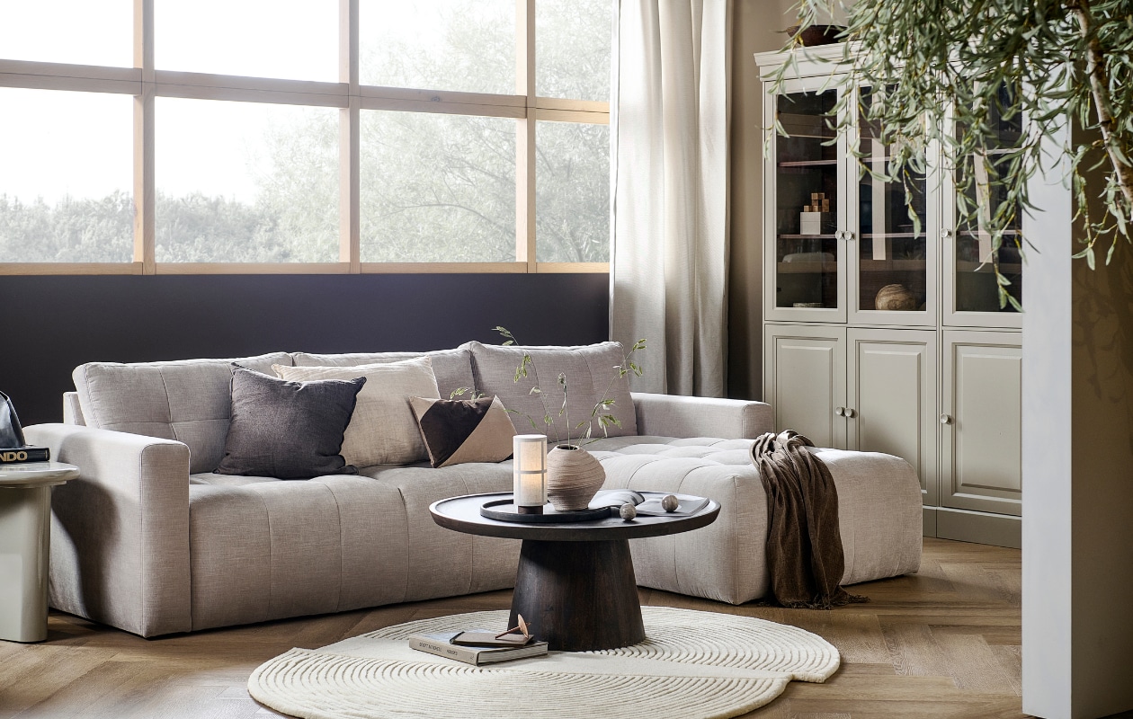 Bank Bar met chaise longue rechts in zand, 280x170x87 cm (bxdxh) € 1749,-, ook met chaise longue aan de linkerkant en in antraciet, groen, roze en warmgrijs. Grenenhouten vitrinekast Chow 2-deurs in Dakargrau, 54x40x215 cm (bxdxh) € 499,-, ook verkrijgbaar als 4-deurs vitrinekast. Walnotenfineer salontafel Coffee a Gogo, 90x40 cm (Øxh) € 499,-. Mangohouten bijzettafel Beach Small in Clay, 64x51x53 cm (lxbxh) € 319,-, ook in 80x80x41 cm (lxbxh).M.m.v. vtwonen.nl/shop (vloerkleed van Bolia, tafellamp van Menu, gestreept kussen van Moos), hm.com (beige aardewerken vaas, bruine plaid), karwei.nl (muurverf Mirre en Warm Brown). Overig privébezit. vtwonen 05-2023 | styling Sanne Ketelaar | fotografie Sjoerd Eickmans
