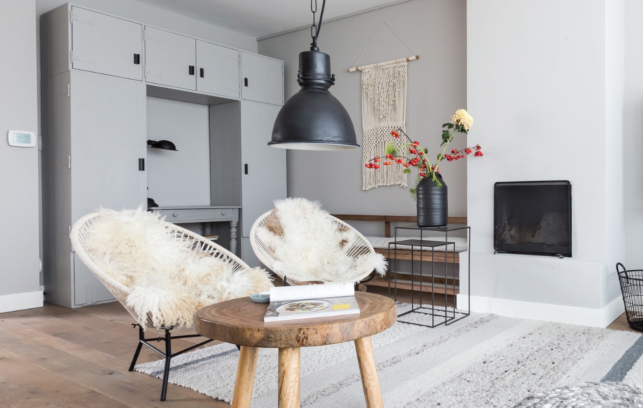 Op de muur: vtwonen Warm grey, per 2,5 liter € 32,95 (www.karwei.nl). Oude Franse eikenvloer in wisselende breedtes per m² € 45,- (www.deoudeplank.nl).  Karpet Fabric grey, Ø 200 cm € 99,-, metalen bijzettafeltjes Bristol, 60x40x30 cm (hxbxd) per set van 2 € 149,- (www.hetkabinet.nl). Poef Ronde, 41x45 cm € 199,-, bijzettafel Boom € 79,95 (www.vtwonen.nl). Antiekzwarte hanglamp Dipper € 174,- (www.hetkabinet.nl). Draadmand large Black € 24,95 (www.hetkabinet.nl). Vintage rotan stoeltje met schapenvacht, gebreid kussen, schaaltjes privébezit. vtwonen 04-2017 | styling Frans Uyterlinde | Fotografie Barbara Kieboom