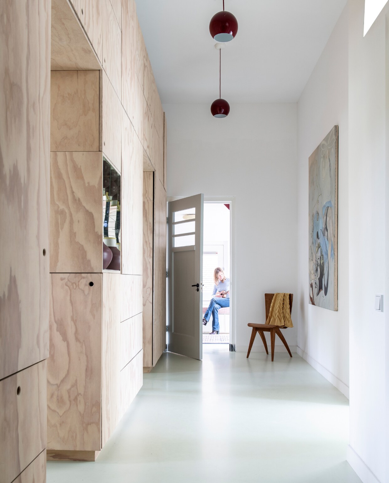 De entree van de oude school. De wandkast van underlayment is een ontwerp van Carmen van der Velde en gemaakt door vormgever/meubelmaker Mischa van der Wekke. In de kast een vaas van Ikea. Schilderij ‘Cowboy’ van Stella de Boo. Rode hanglampen Topan van Verner Panton. De stoel is een cadeau. Vloer ComfortFloor Pro van Sika in de kleur S1010/GY05.Wie: Clementine van Wijngaarden (49, journalist), Luc (17) en Kate (15) vtwonen special 03-2020  | productie InsideHomePage | styling Kristel de Jong | fotografie Louis Lemaire
