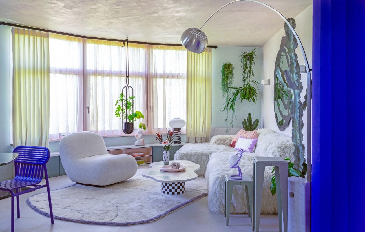 Gordijnen Ado Goldkante. Lage wandkast op maat gemaakt. Organische vaas Hannah Simpson Studio. Spiraallamp vintage. Plantenhanger Atelier Haussmann. Blauwe stoel Petite Friture. Fauteuil Chelsea BoConcept. Vloerkleed eigen ontwerp, handgemaakt in Marokko. Op maat gemaakte salontafel Minerva Artlab. Vaas Studio Arhoj. Roze bord Moustache. Bank Pyllow Mycs, schapenwollen bekleding zelfgemaakt. Bijzettafels Chamfer Wye Design. Paarse oog-lamp mattina moderna. Vloerlamp Arco Flos. vtwonen binnenkijken special 121-2022 | productie & fotografie Anne Catherine Scoffoni