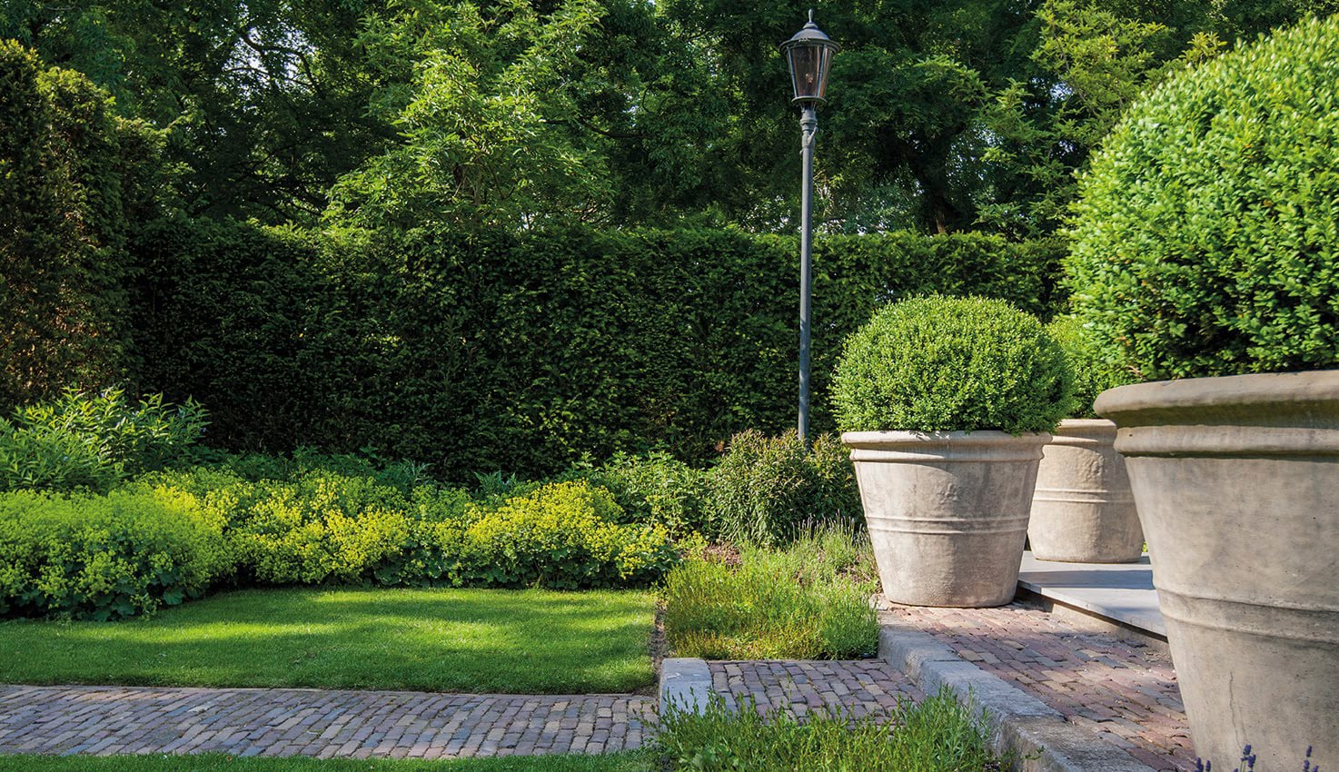 Vaste en losse elementen in perfecte harmonie met elkaar. De klinkers en de treden passen mooi bij de bloempotten van Italiaans aardewerk. Hovenierscentrum De Briellaerd