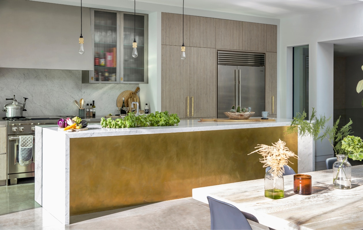 De middagzon krijgt alle ruimte in de op maat gemaakte keuken. Natuurlijke materialen als hout, metaal en steen verbinden de ruimte met buiten. Op de vloer ligt gepolijst beton. Keuken van Matrix Design, hanger van Buster + Punch. ‘De keuken is mijn favoriete ruimte. Het was de eerste kamer die ik ontwierp. Ik wilde dat het een gastvrije familieruimte werd.’ vtwonen 01-2020 | fotografie Rei moon/living Inside