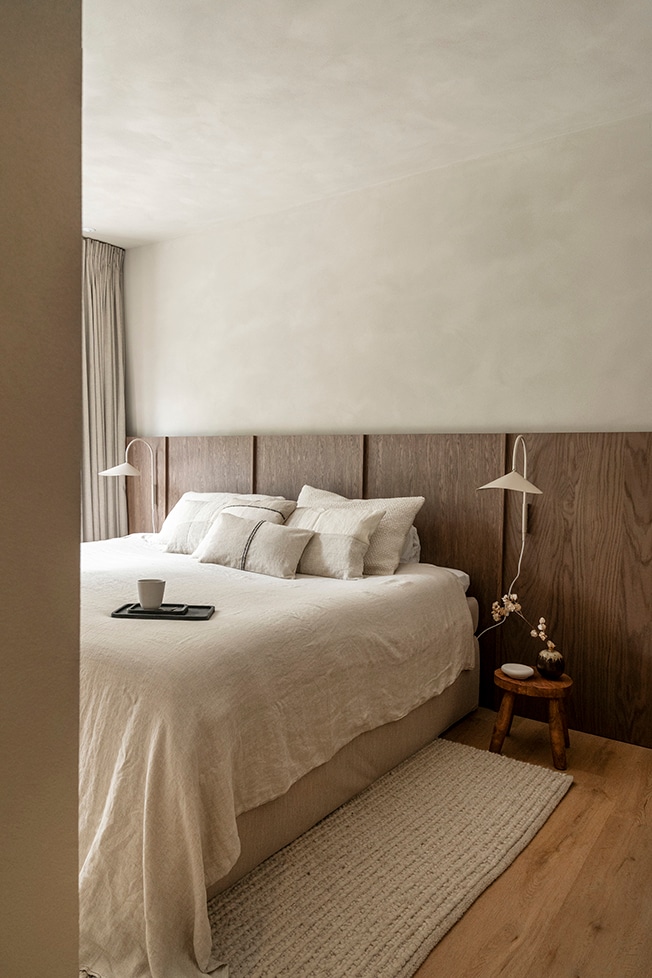 Het door Van Zon Interieurbouw op maat gemaakte hoofdbord loopt over de hele breedte van de slaapkamer. De lampjes aan weerszijden van het bed zijn van Ferm Living. Het beddengoed is van Zara Home. Wanden en plafond zijn afgewerkt met dezelfde kleur microtopping door Dofine. Fotografie Muk van Lil