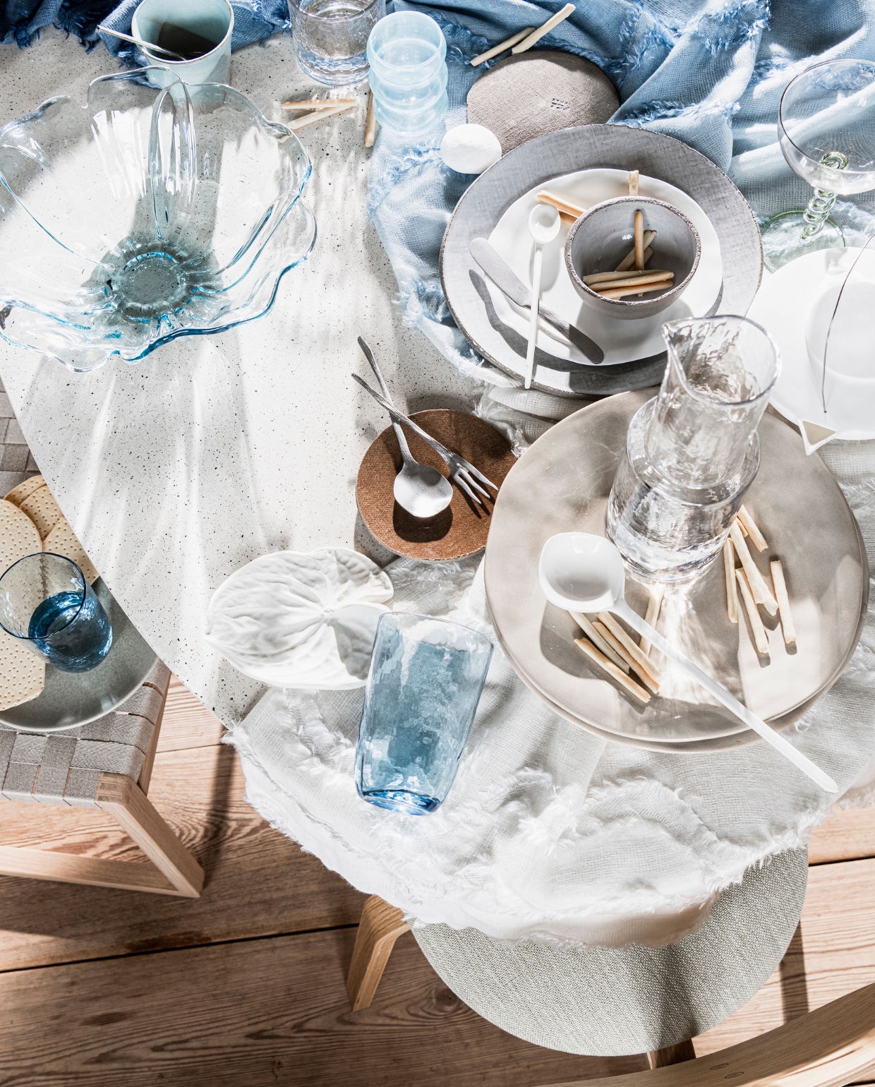 Tafel € 2190,- (lanenahome.com). Tafelkleed gemaakt van stof Temco van Osborne &amp; Little, per meter € 180,-(wva.nl). Lichtblauwe mok € 12,95, lichtblauw glas € 9,95, cocktailglas met gedraaide poot € 15,95 (anna-nina.nl). Transparant gehamerd waterglas € 5,99, blauwe plastic schaal in vorm van bloem € 5,99, beige organisch gevormde borden, per stuk € 11,99, karaf van gehamerd glas € 15,99 (zarahome.com). Grijs cementen bord € 13,50, wit porseleinen zoutvaatje in vorm van kiezel € 15,50, zachtgrijs bord met cementen rand € 34,- wit porseleinen bord in organische vorm € 29,-, grijze kom met cementen buitenkant € 13,50, zilveren bestek, per stuk vanaf € 7,75, bruin bord met cementen onderkant € 13,50 (serax.com). Witte keramieken lepels, per stuk vanaf € 9,90 (letoile.store). Wit keramieken blad € 109,- (annekebruin.nl). Blauw gehamerde glas € 15,50 (brostecopenhagen.com). Houten eetkamerstoel met beige gevlochten zitting van Fredericia € 1001,-, houten eetkamerstoel met stoffen zitting van Menu vanaf € 450,- (designtales.nl). vtwonen 08-2020 | styling Danielle Verheul | fotografie Sjoerd Eickmans | assistentie Niels Kist, Meike LintHorst | maatwerk Meta Poulain