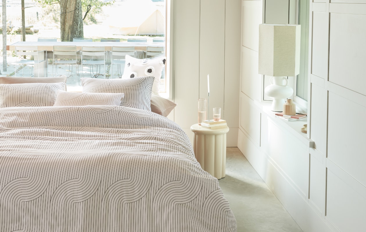 vtwonen collectie (Katoenen dekbedovertrek Stripe and Eye, 140x200/220 cm € 59,95, 200x200/220 cm € 109,95, 240x200/220 cm € 119,95, katoenen kussen Stripe and Eye, 50x50 cm € 44,95). M.m.v. vtwonen.nl (kussenhoezen en dekbedovertrek gebruikt als onderlaken in Earth Pink van vtwonen), loods5.nl/design (stenen kruk, tafellamp met kap), loods5.nl (vloerkleed), designtales.nl (tafellamp), letoile.store (mok), sissy-boy.com (kandelaar), polspotten.com (vaas). Overig privébezit. vtwonen 04-2023 | productie Tanja Saarberg | styling Danielle Verheul | fotografie Richard Smit