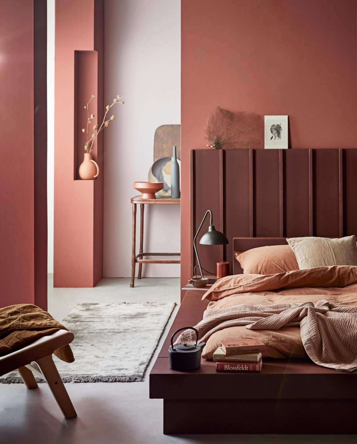 vtwonen collectie (Muurverf Red Earth (voorste wanden en kolom), Washed Lilac (achterwand), lakverf Terra (bed en headboard)) M.m.v com-anders.nl (op maat gemaakt headboard en bed), vtwonen.nl (tafellamp Orion, beddengoed Natural Stone in kleur Terra, roze sprei en stoel van hout en leer uit de vtwonen collectie, groot bord met gezicht van Ferm Living), nordal.eu (terracotta vaas met oor, vloerkleed, grote terracotta schaal, theepot, karpet), iblaursen.com (quilt op stoel, roze linnen kussen), maisonnl.com (bruin rond leren potje, bruin boek). Overig privébezit. vtwonen 04-2020 | productie Tanja Saarberg | styling Cleo Scheulderman | fotografie Jeroen van der Spek
