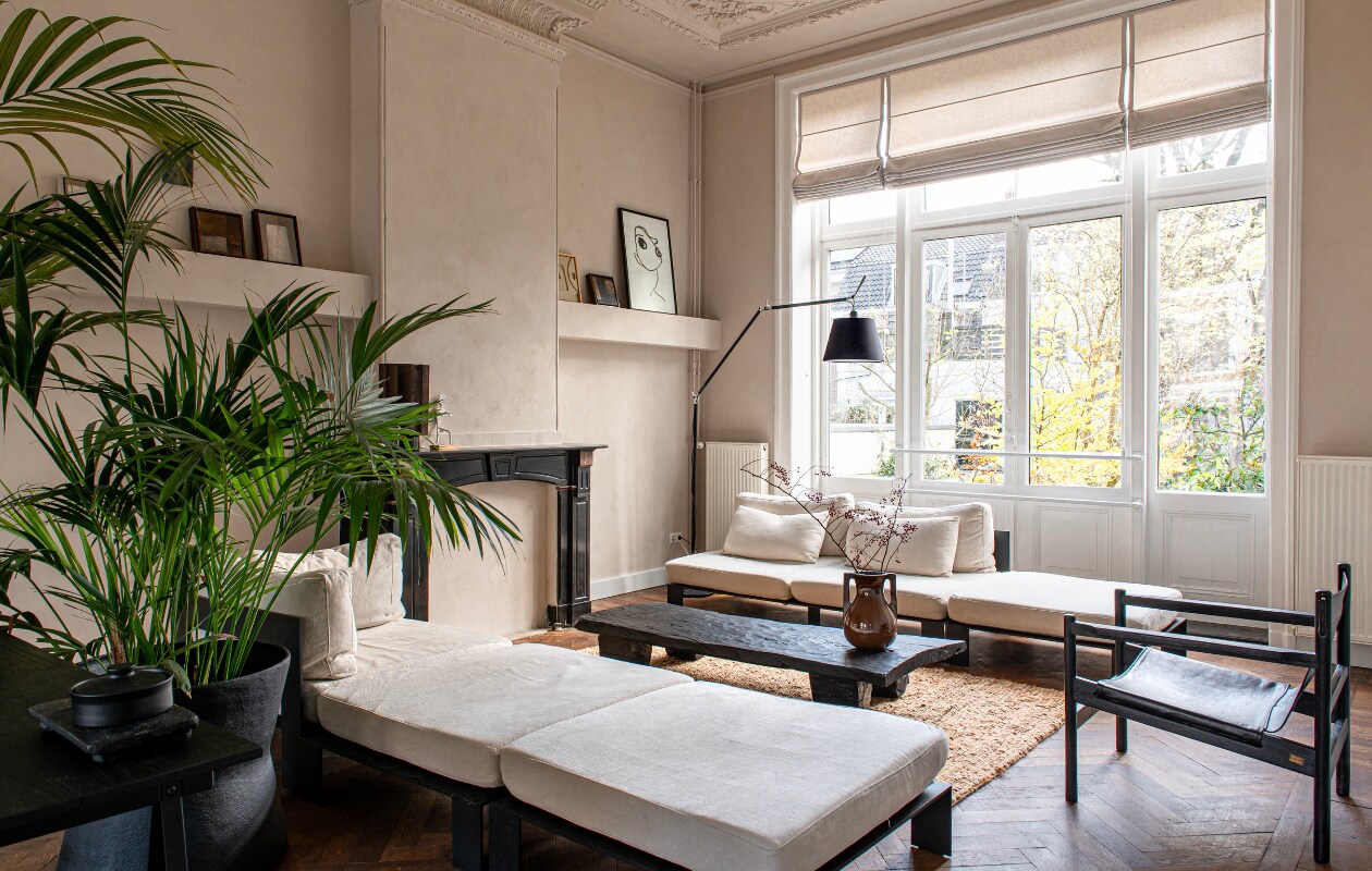 Vloerlamp Artemide. Portret rechts Loods 5, daarnaast en links van de schouw werk van Eef Sanders via JAS, reliëf van Edith Beurskens. Sisal vloerkleed Urban Nature Culture, schaal met deksel H&amp;M Home. Bank van Serax, safaristoel van BePureHome, Naga salontafel uit India, grote plantenpot en vaas Mississippi, alles via JAS. Raambekleding onbekend. vtwonen binnenkijken special 131-2024 | productie De Binnenkijkers | styling Jeske Weel | fotografie Caroline Coehorst