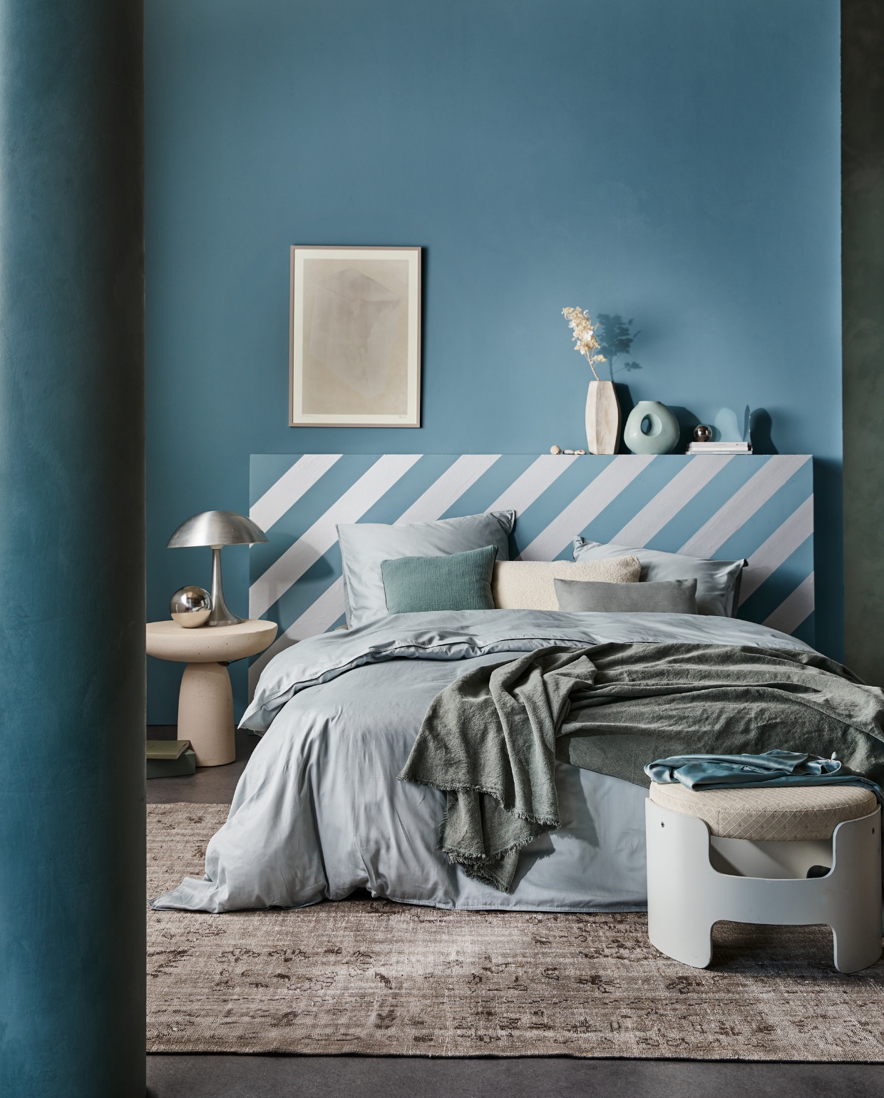 Behangstrook Silver, 10,66 cm (b), rol van 10 m € 12,99.M.m.v. suite702.nl (satijnen beddengoed in Glacier Grey), neeflouis.nl (poef), edha-interieur.nl (bijzettafel), pietjonker.nl (zilveren lamp), urbannatureculture.com (vazen), rozenkelim.nl (vloerkleed), theposterclub.com (ingelijste poster), zarahome.com (linnen plaid, kussens), vtwonen.nl (muurverf Old Blue). Overig privébezit. vtwonen 02-2023 | productie tanja saarberg | styling cleo scheulderman | fotografie jeroen van der spek