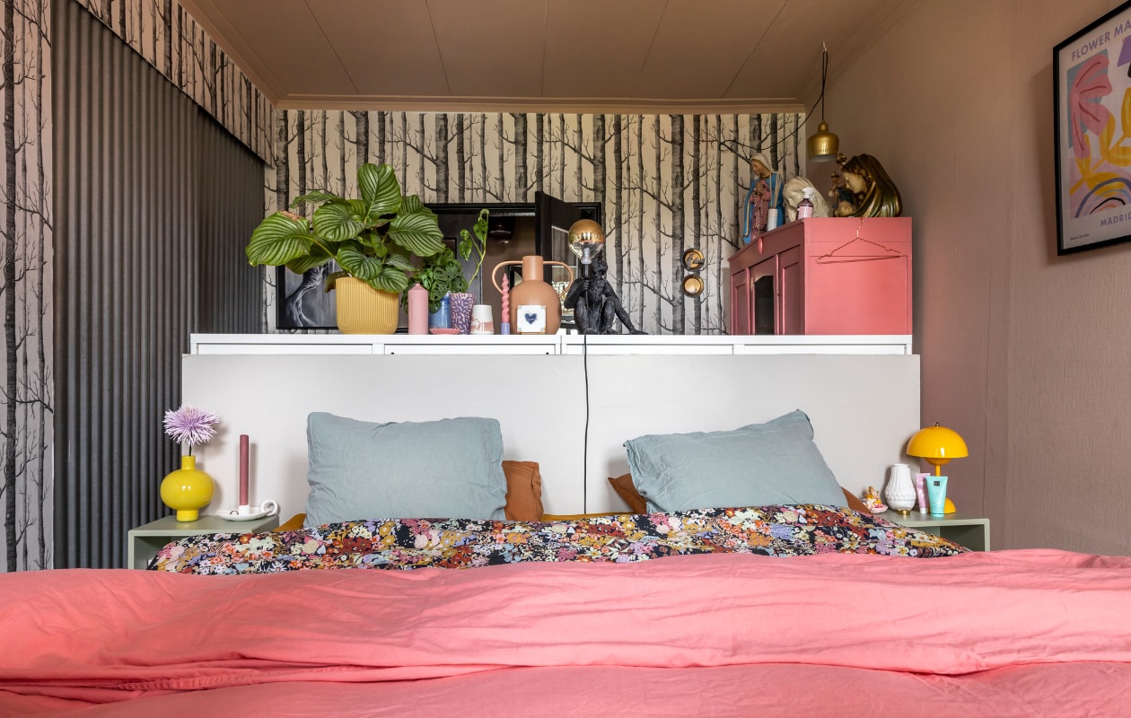 Bloemenbeddengoed Crisp, overig beddengoed Wehkamp. Gele vaas en kandelaar ’t Pothuys, gele bloempot Elho, roze vaas Foekje Fleur, blauwe pot en roze/beige potje Prchtg, lila vaas Huis van Bloemen. Lila kandelaar met roze kaars Hay, tegel Storytiles. Nachtkastje Ikea, behang Cole &amp; Son. Verf plafond Setting Plaster van Farrow &amp; Ball, verf roze kast Flowerbulb van Flexa. vtwonen binnenkijken special 131-2024 | fotografie Henny van Belkom