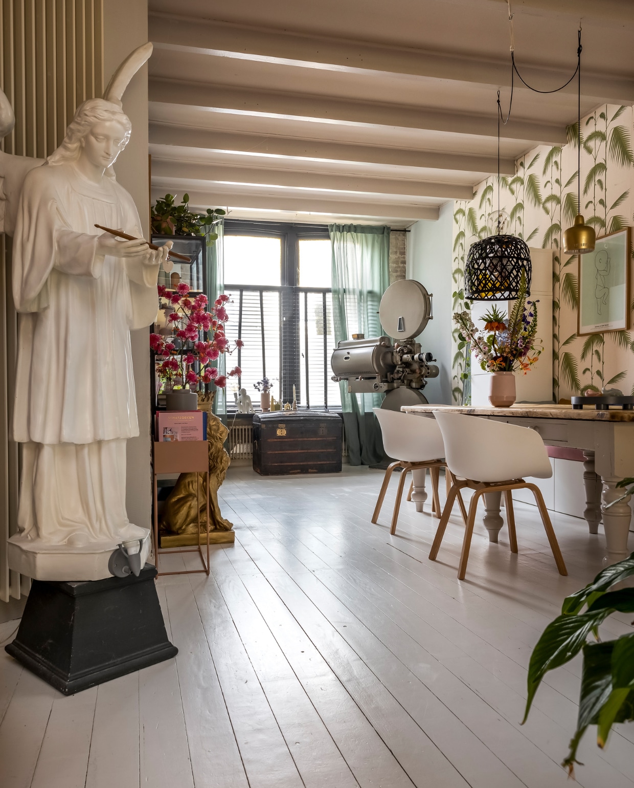 Stoelen Hay, roze vaas Hella Duijs, poster The Birth Poster, roze bloemen Huis van Bloemen. Roze plantenbox Ferm Living, blauwe tray Muuto, gordijnen Ikea, jaloezieën Kwantum. Engel oud etalagemateriaal, kist erfstuk, filmprojector uit de bioscoop in Vlissingen. Gouden leeuw via een veilinghuis. Behang Cole &amp; Son. Vloer houten planken geverfd met witte betonverf Karwei. Muurverf Borrowed Light en verf plafond Elephant Breath van Farrow &amp; Ball. vtwonen binnenkijken special 131-2024 | fotografie Henny van Belkom