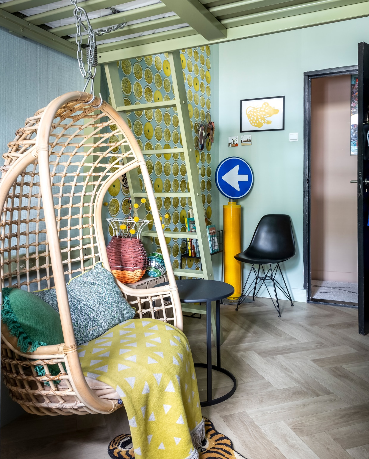 Hoogslaper Ikea, geverfd in Sir Lutyens Sage van Little Greene. Hangstoel en langwerpig kussen HKliving, plaid de Bijenkorf, stoel Vitra, tegels Storytiles. Poster Hello Mado. Insecten Studio Roof, discobal La Bella Cucina. Kleed en rond groen kussen Sissy-Boy, bijzettafel Kwantum, vaas Femkeido, rek onbekend. Verkeersbord van straat. Behang Cole &amp; Son. Muurverf Teresa’s Green en verf op deur Setting Plaster van Farrow &amp; Ball. vtwonen binnenkijken special 131-2024 | fotografie Henny van Belkom
